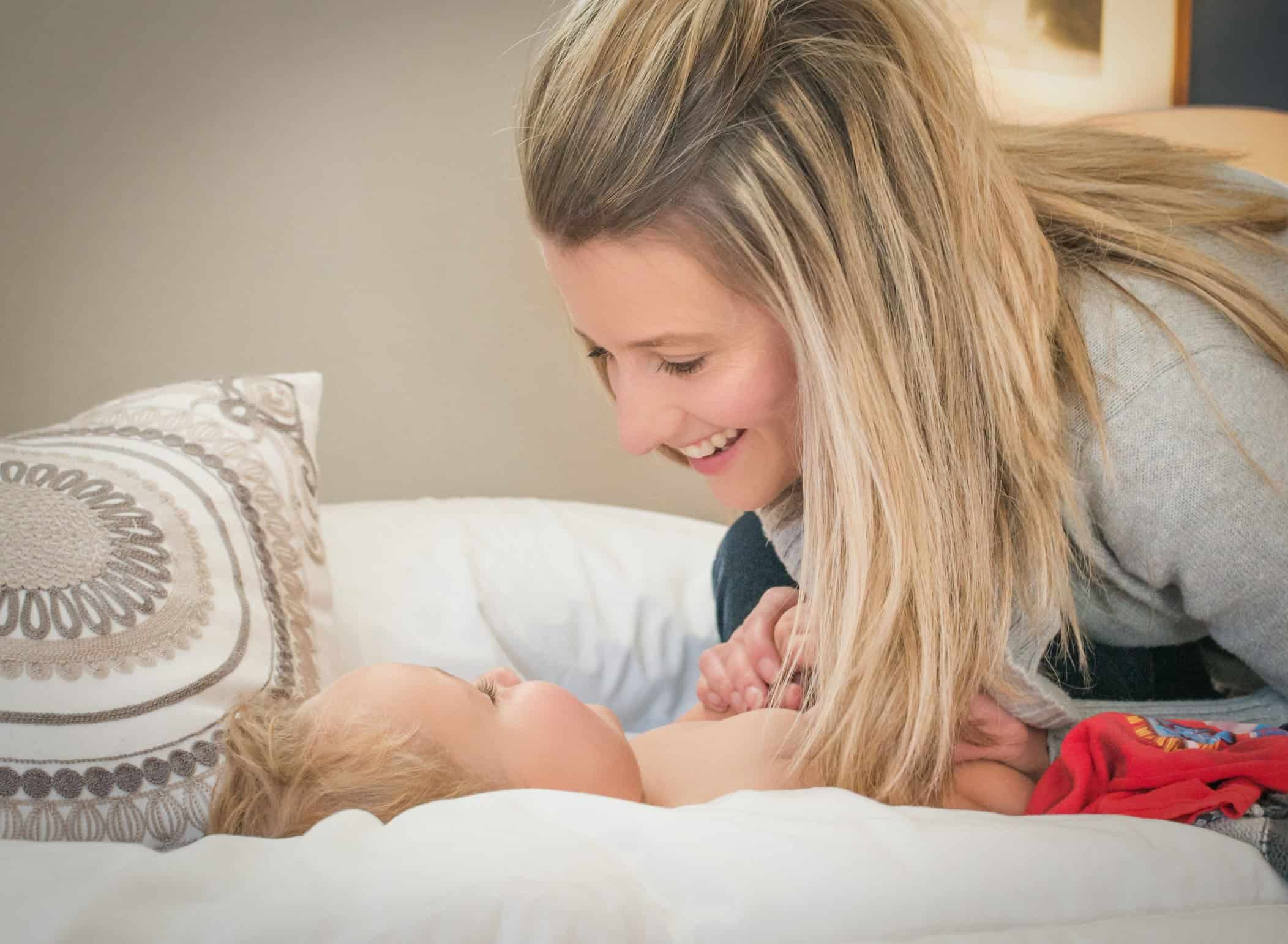 Mom looking at baby son on bed holding his hands