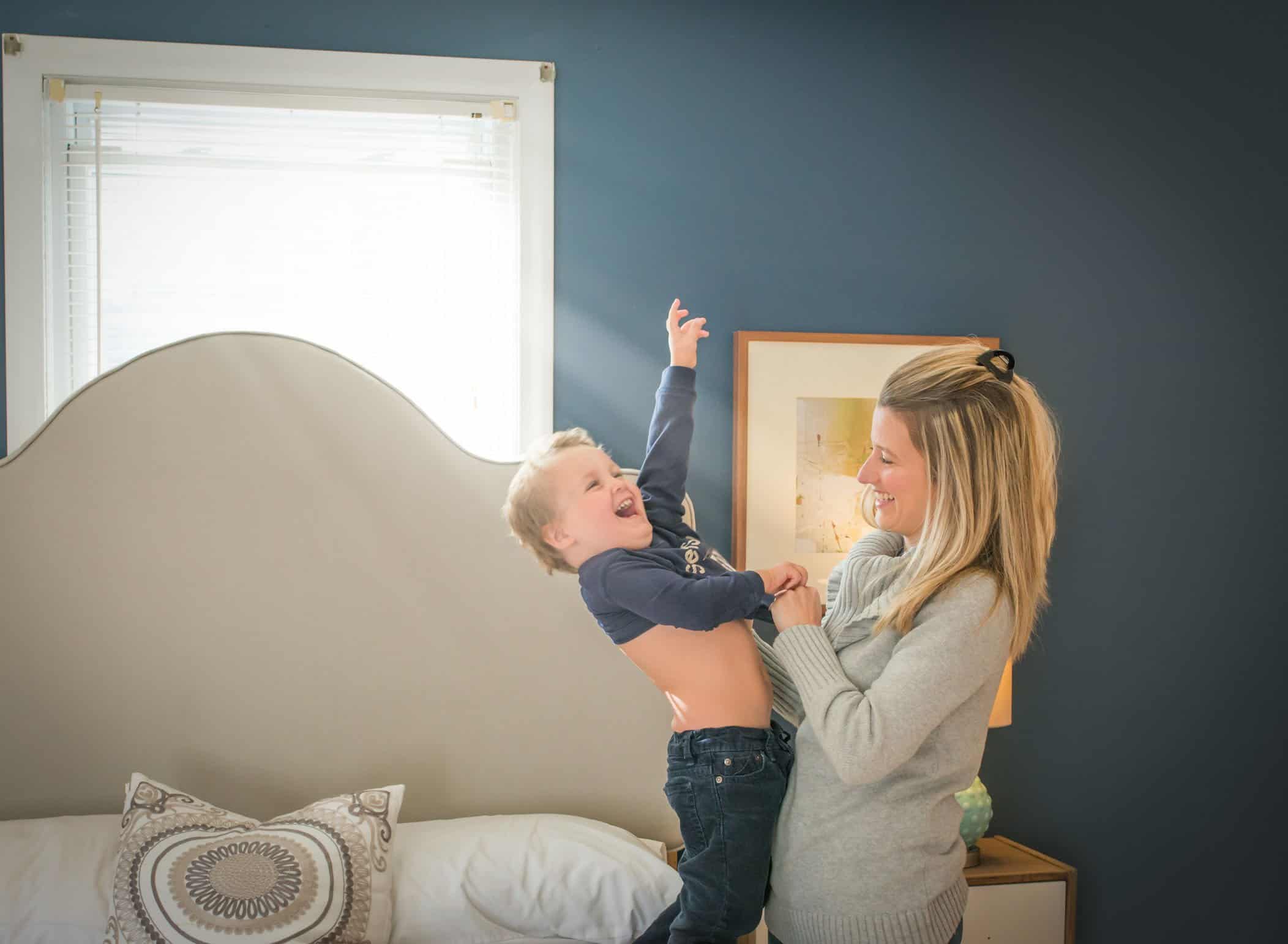 Mom helping toddler son change his shirt laughing