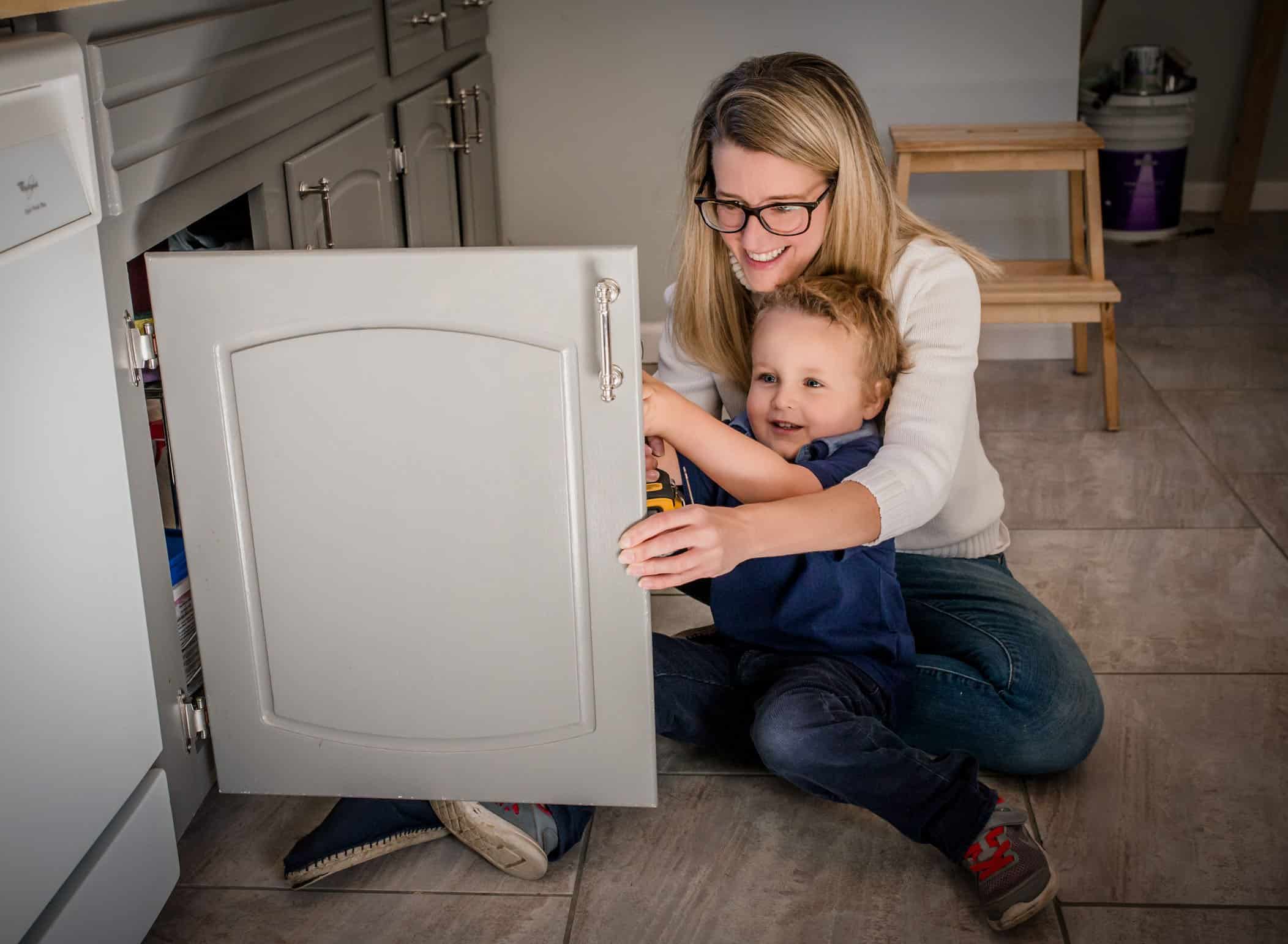 Mom & toddler son fixing cabinet in kitchen