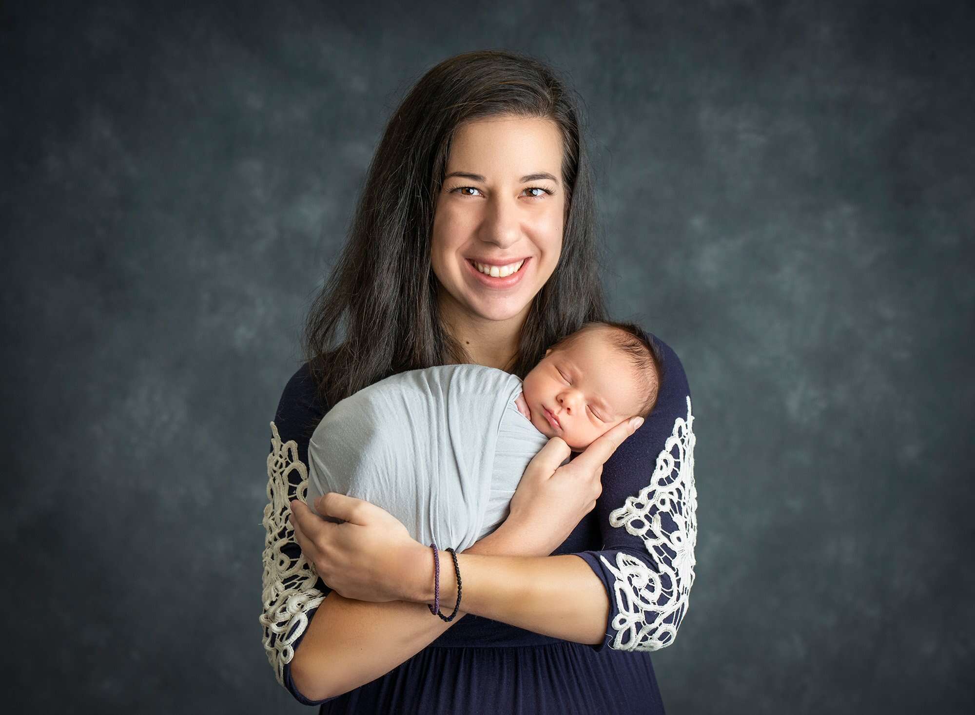 mom looking down at newborn baby boy swaddled in gray