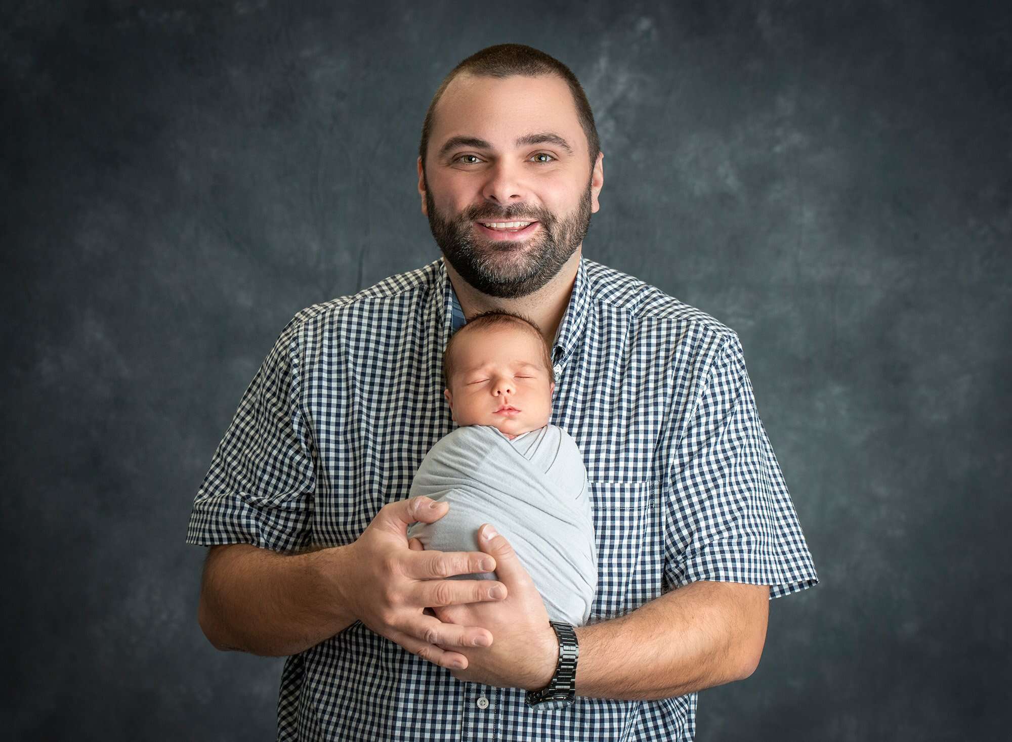 dad cradling newborn baby boy swaddled in gray