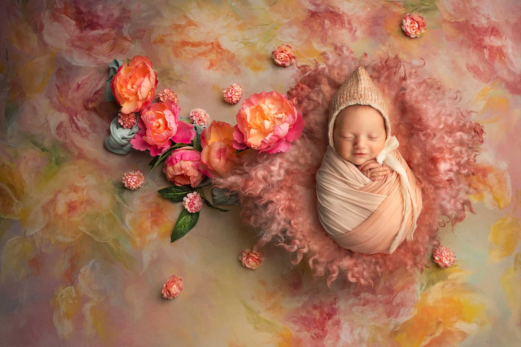 how to prepare for newborn photoshoot Glastonbury CT Adorable smiling newborn wearing a bonnet, wrapped in warmth on a vintage rose backdrop of oranges, pinks, and yellows.