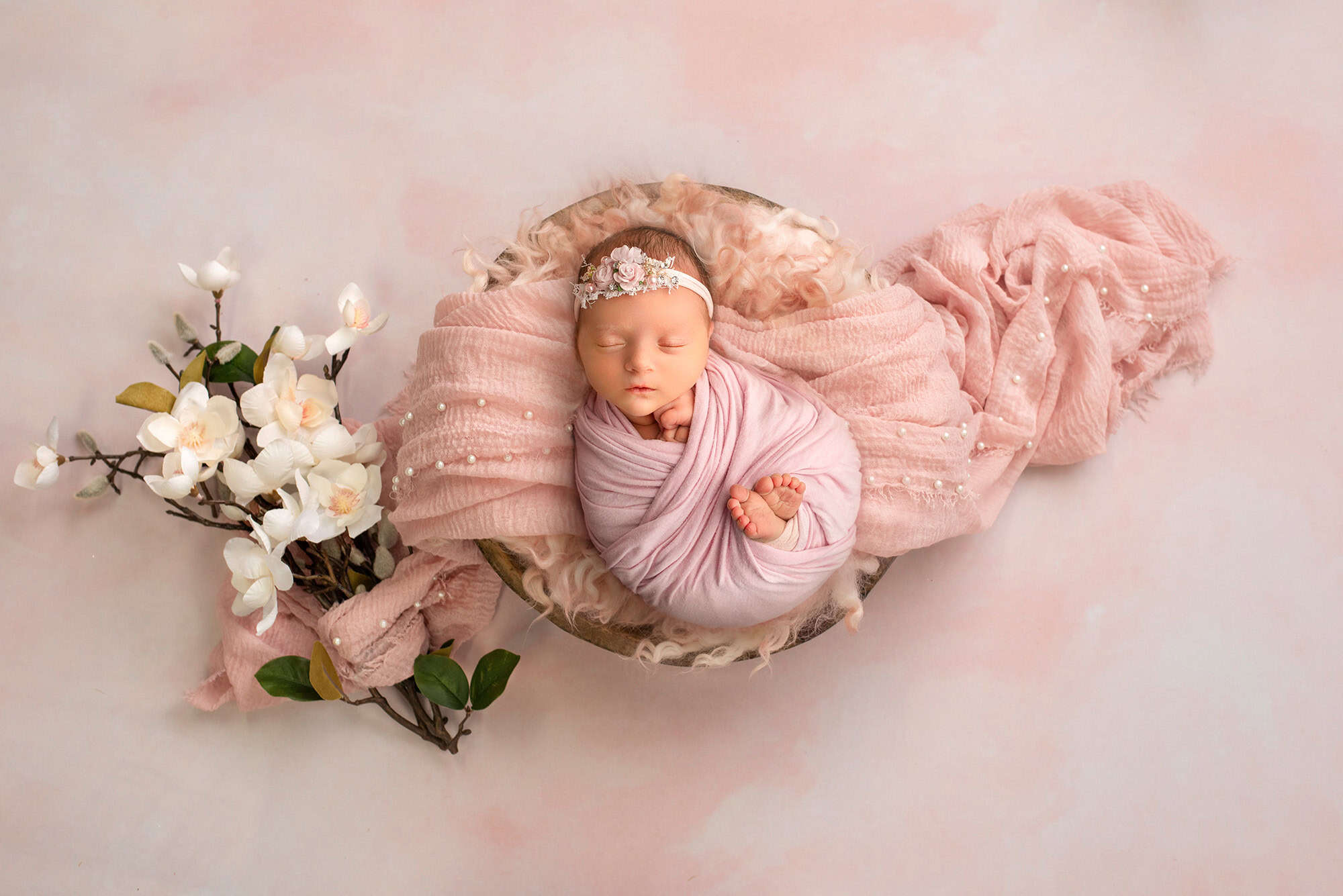 Sweet baby with tiny toes peeking out, nestled beside a bouquet of magnolias in a simple, heartwarming photograph
