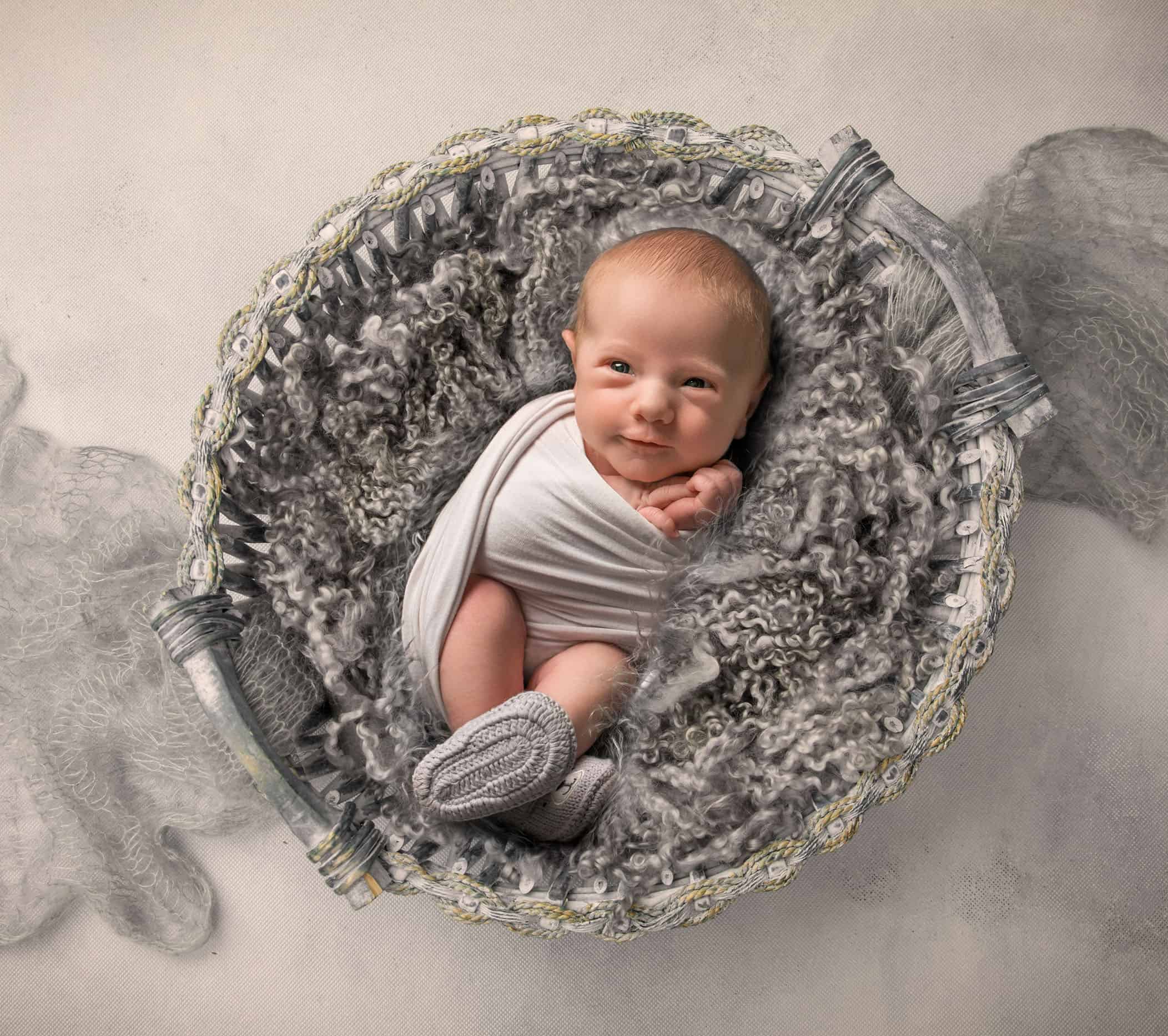 newborn baby boy swaddled in grey fluff basket with grey booties on his feet