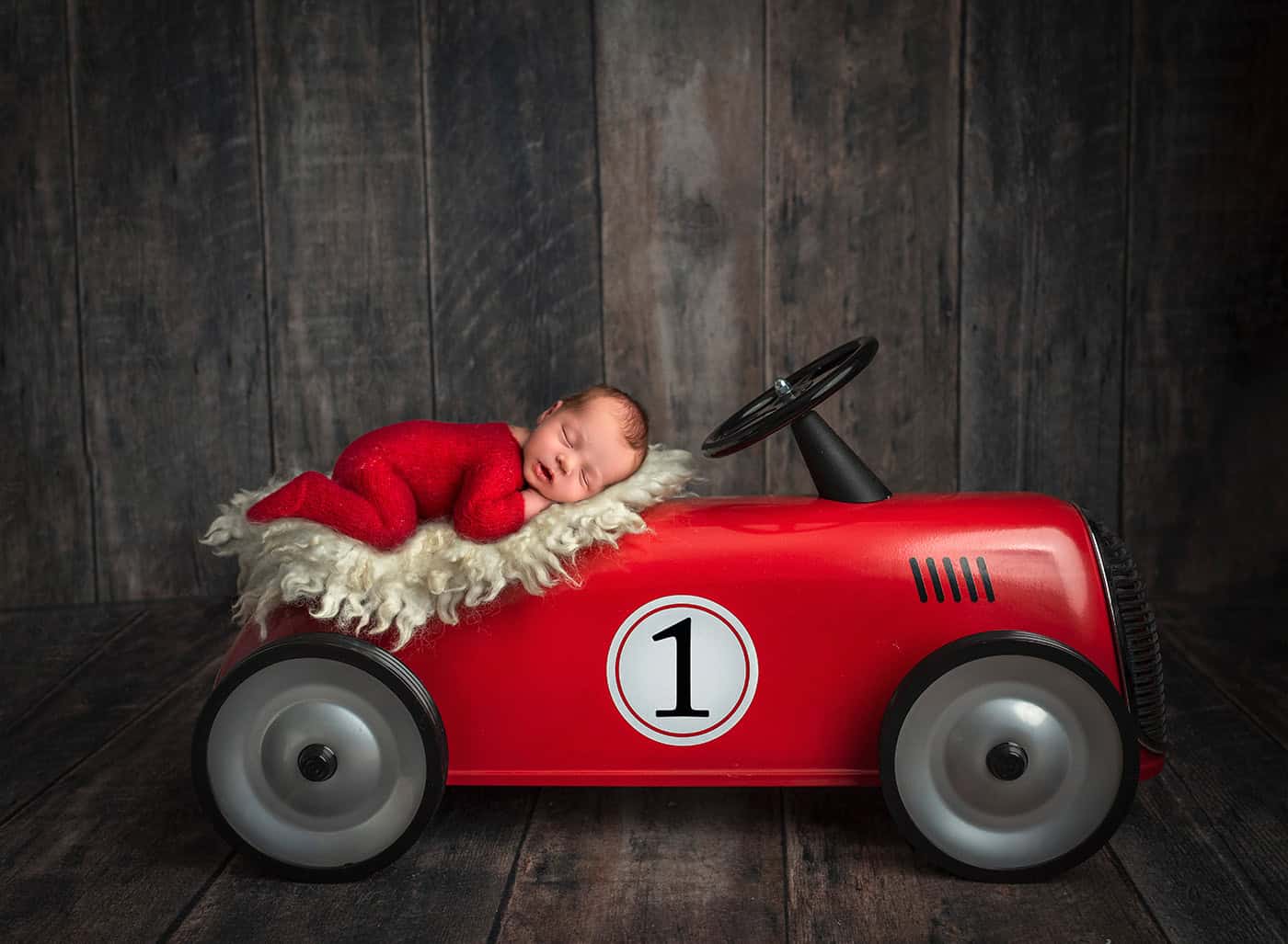 newborn napping into the world of car racing on a vibrant red race car
