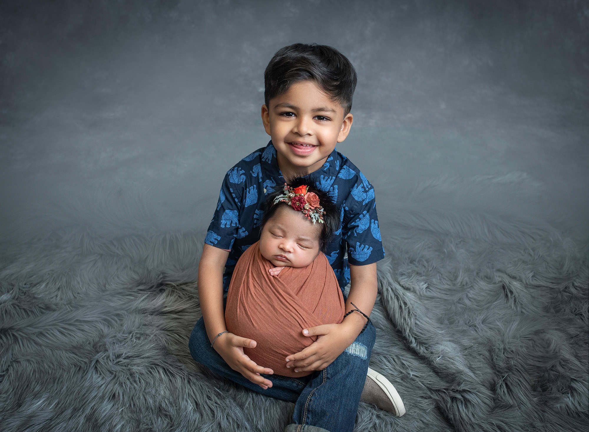 Meaningful Newborn Photos young boy cradling newborn baby sister swaddled in rustic orange