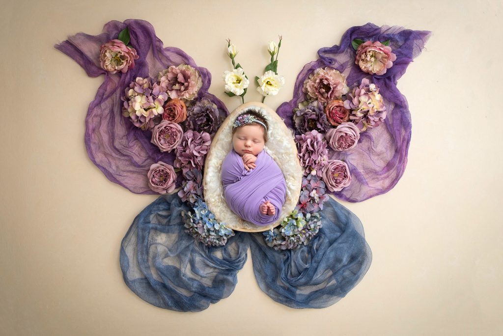 Newborn Photos with Butterflies sweet newborn baby girl asleep swaddled in purple inside of a butterfly