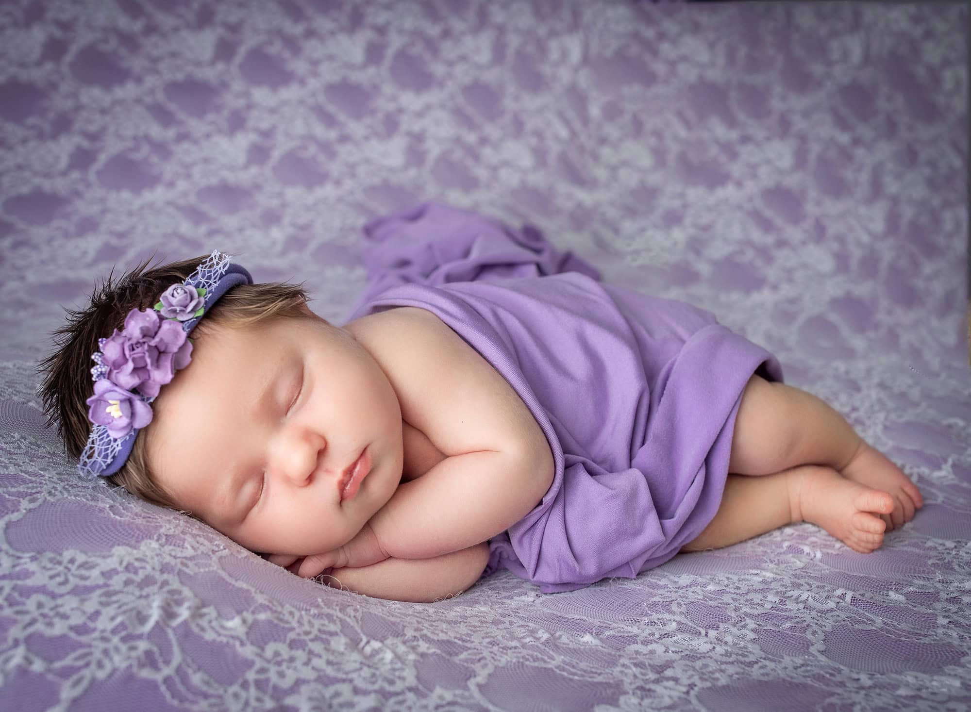newborn baby girl asleep on laced purple blanket wearing purple headband