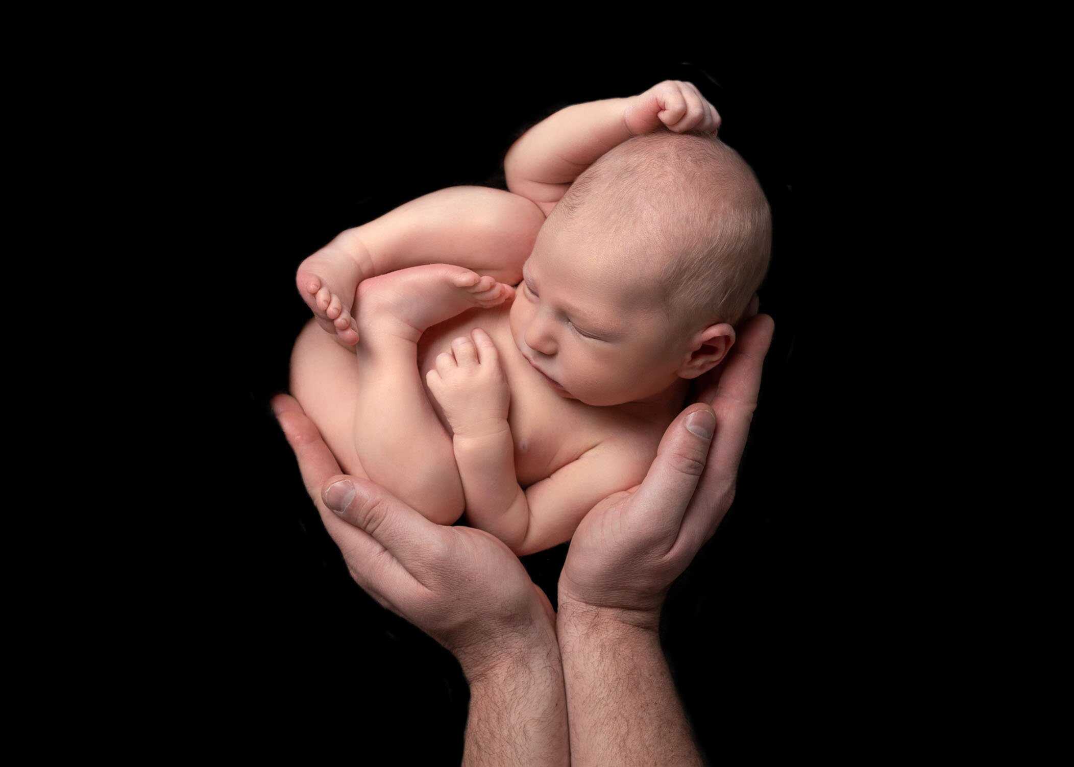 newborn boy sleeping in his father's hands on black