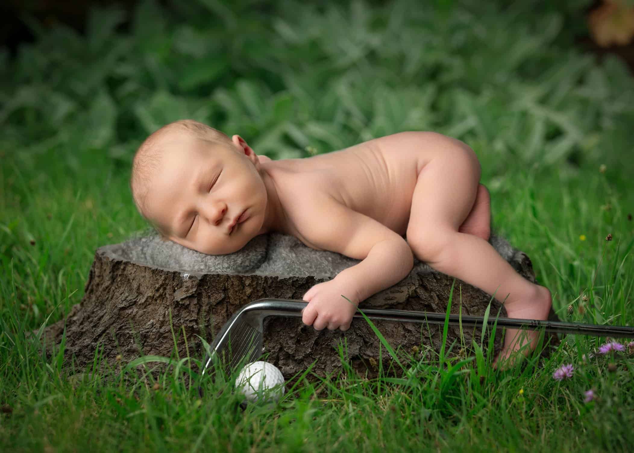 newborn boy sleeping on log outside with a golf club in his hand and golf ball below