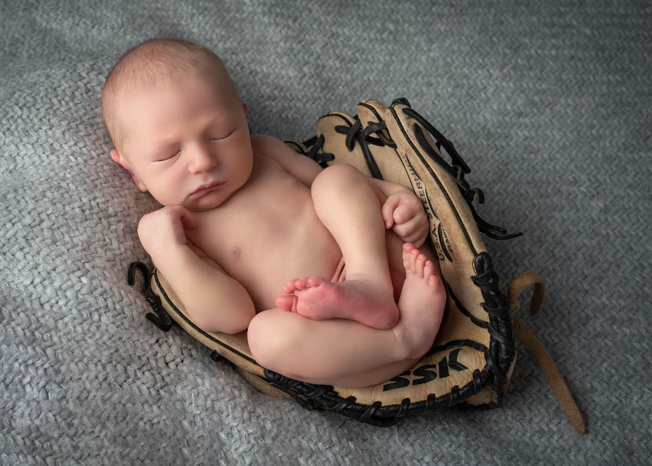 newborn baby boy sleeping in baseball glove