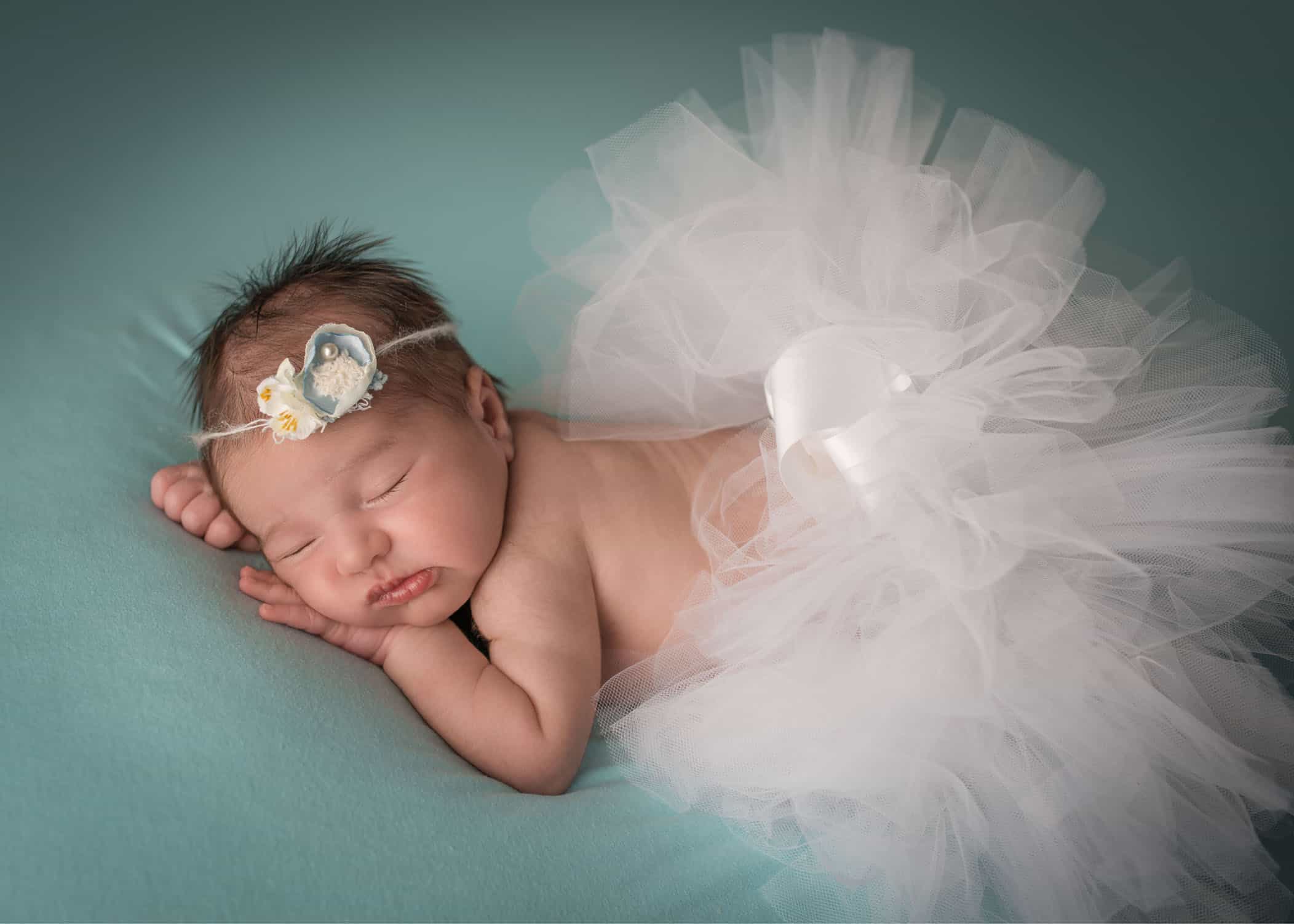 Newborn girl in white tutu on teal background