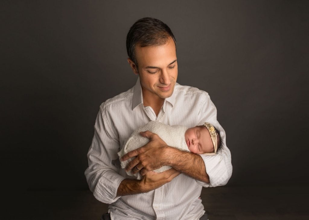 Dad holding newborn daughter in arms smiling at her