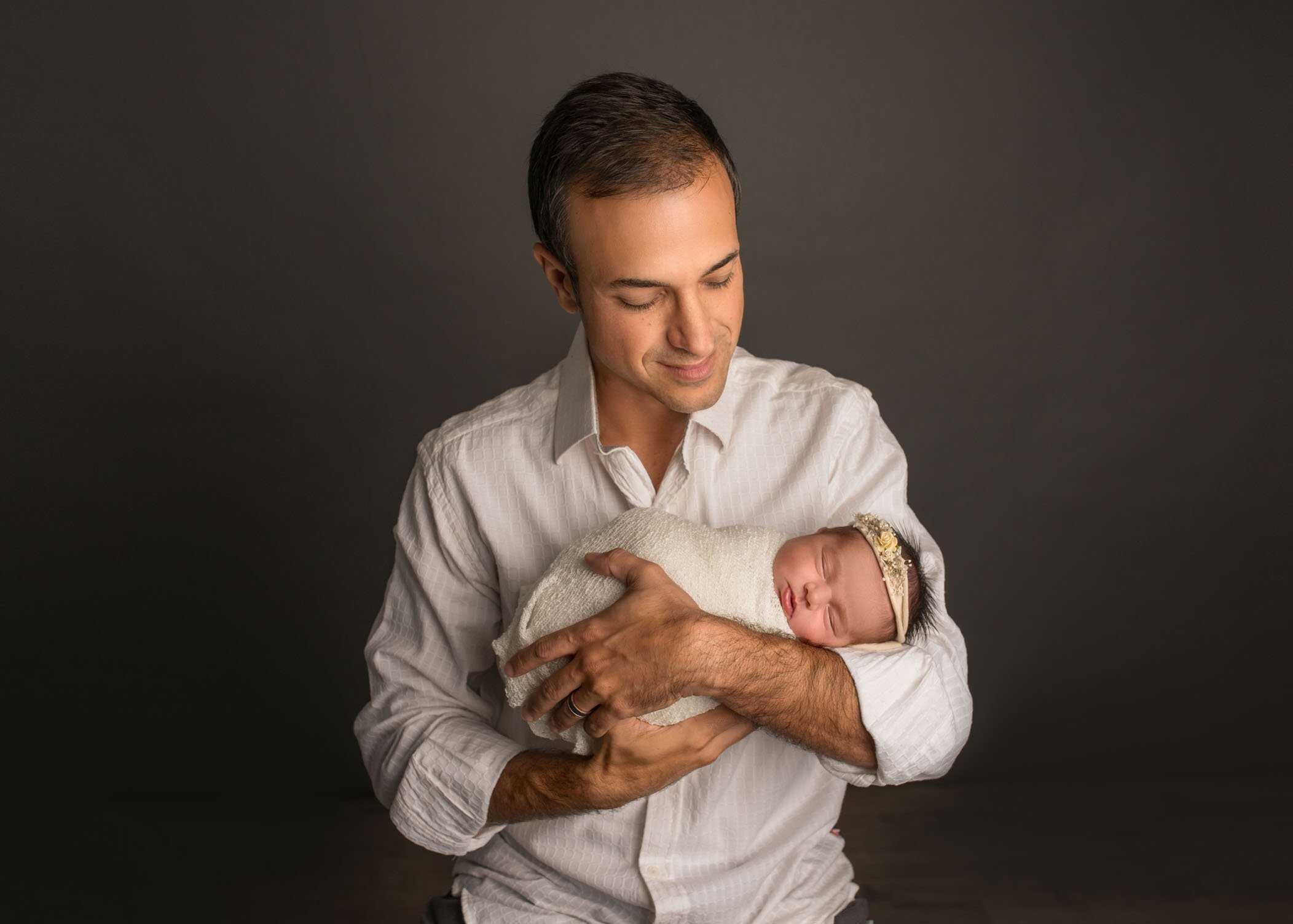 Dad holding newborn daughter in arms smiling at her