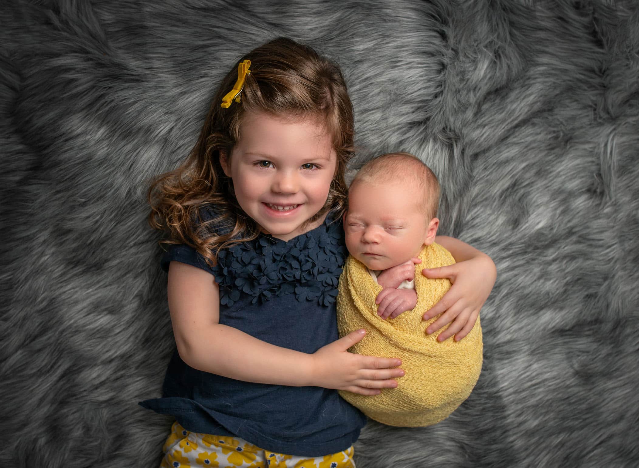 3 year old big sister holding swaddled baby brother while he sleeps