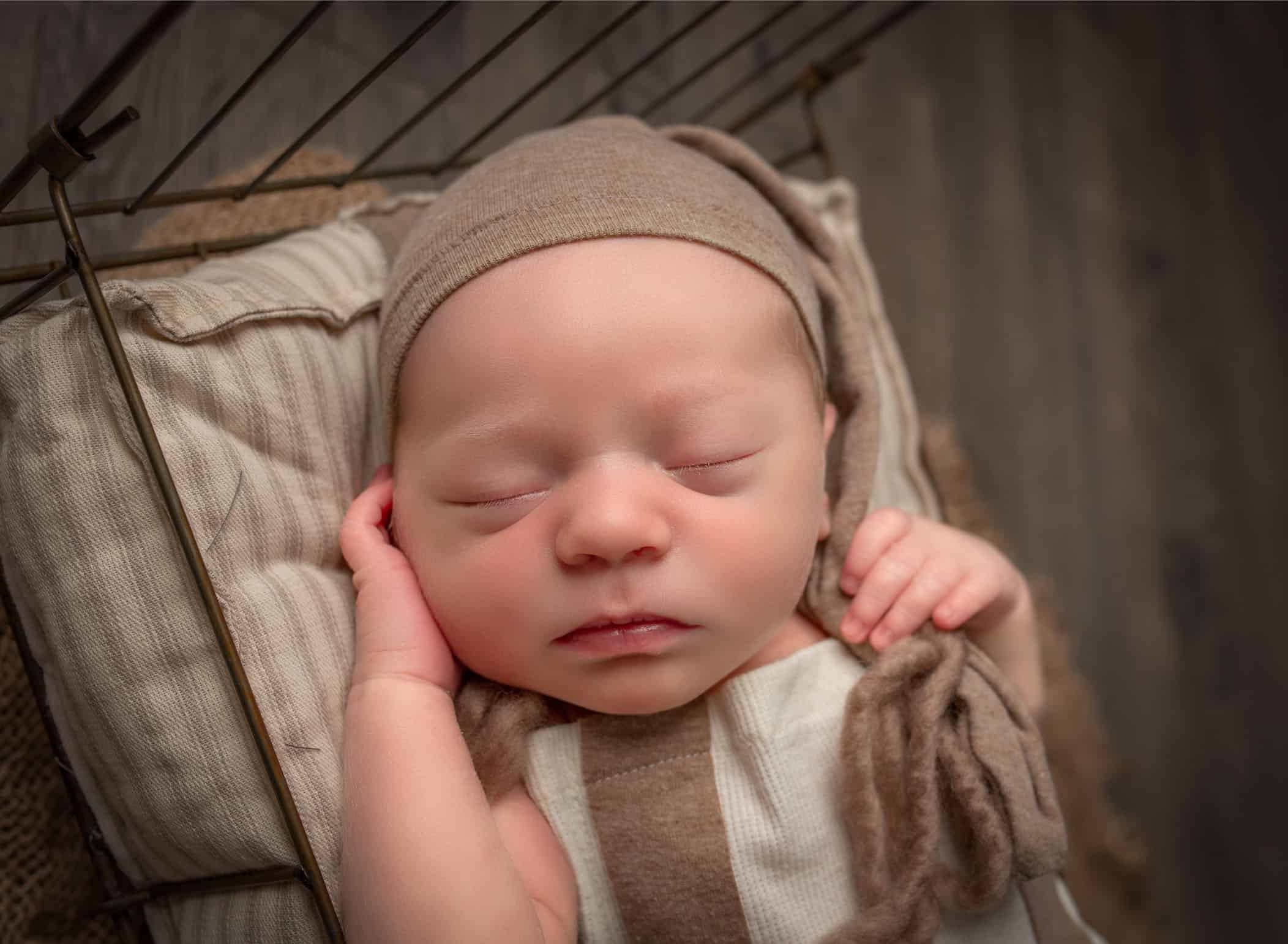 Newborn baby sleeping with nite cap on in old fashioned wire bed