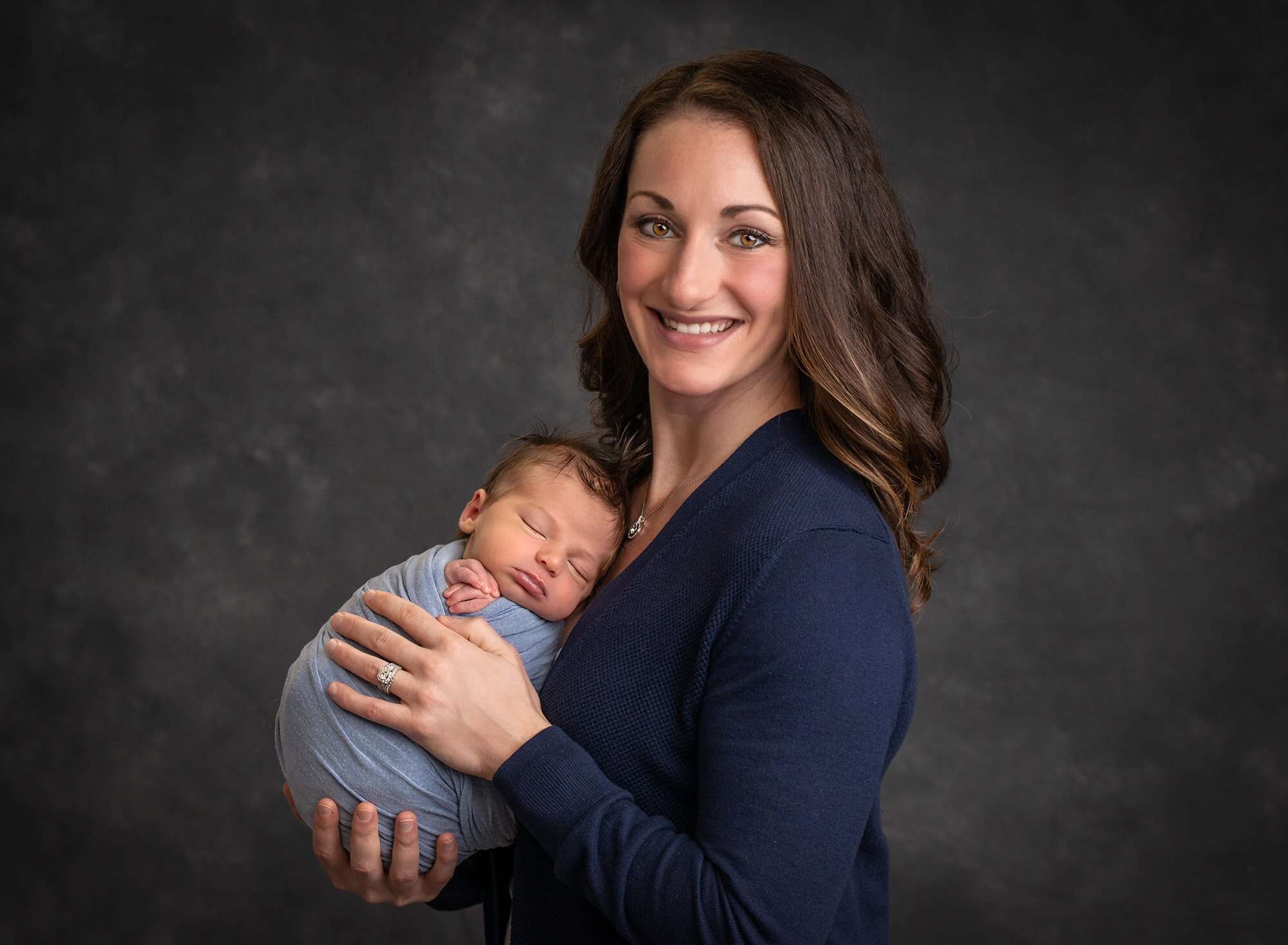 new mom holding asleep newborn baby boy swaddled in blue