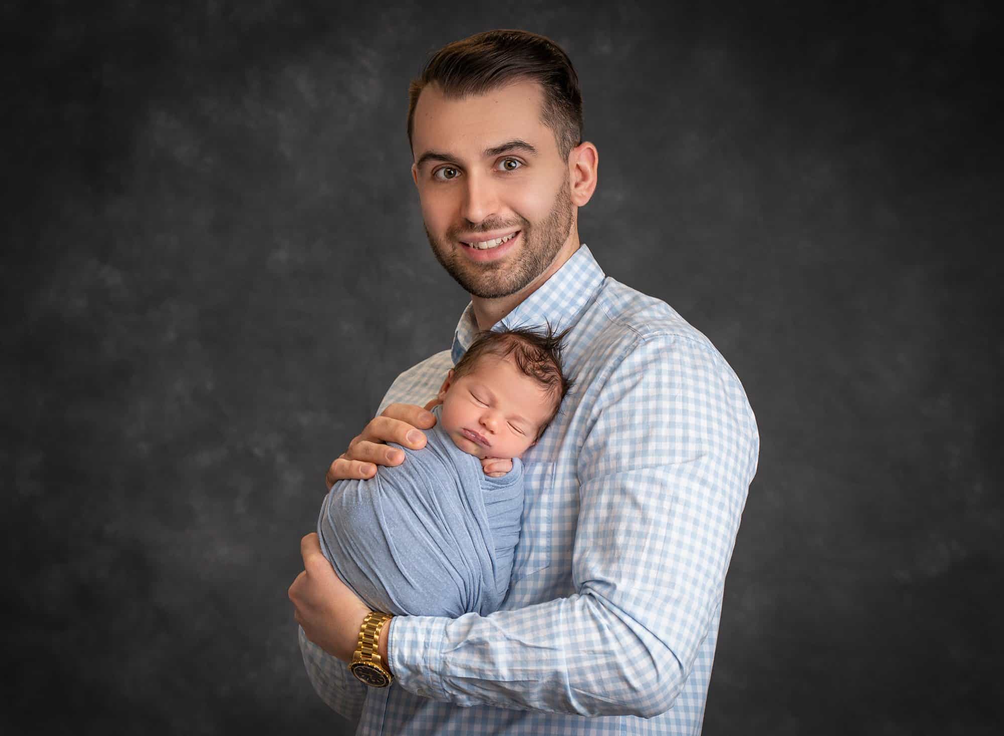 dad holding sleeping newborn baby boy swaddled in blue