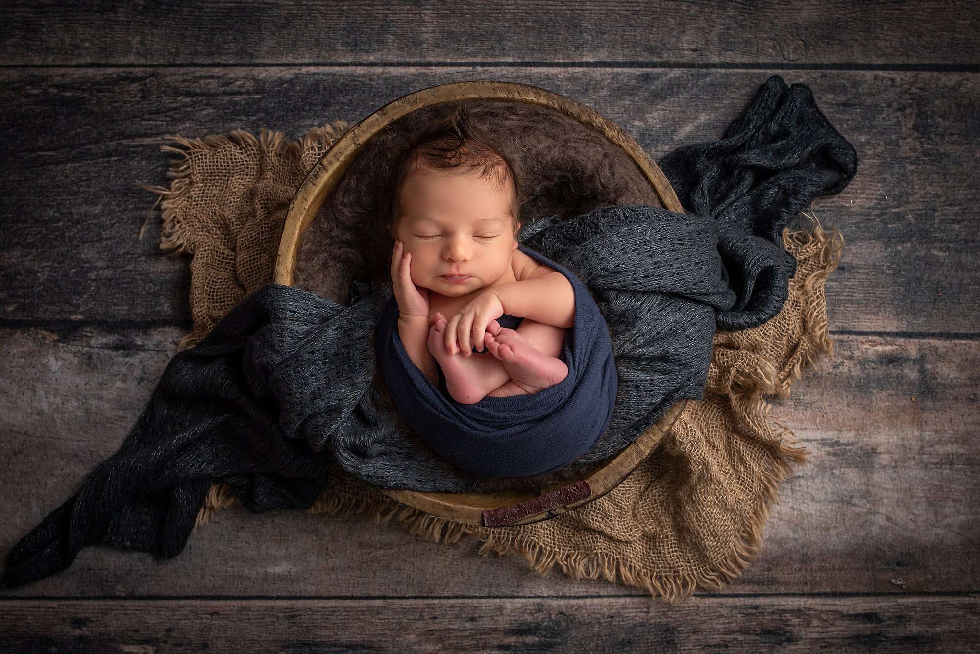 newborn baby boy swaddled in blue asleep in wooden bowl