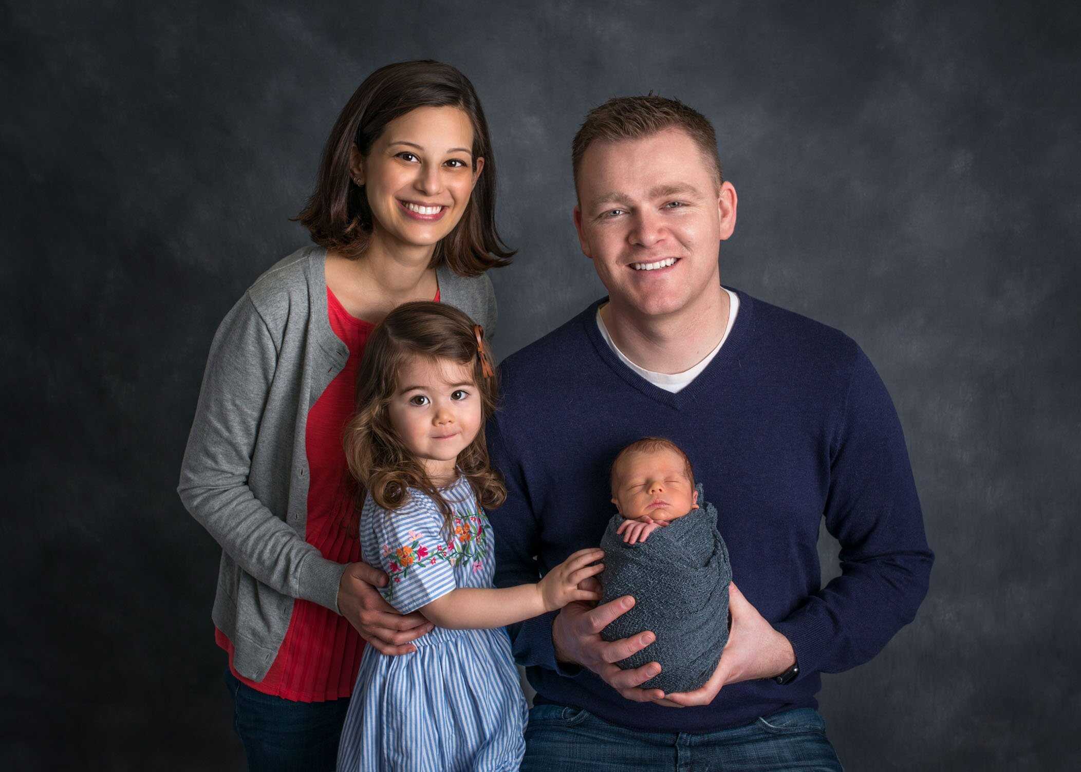 Mom Dad and toddler daughter posing with newborn son