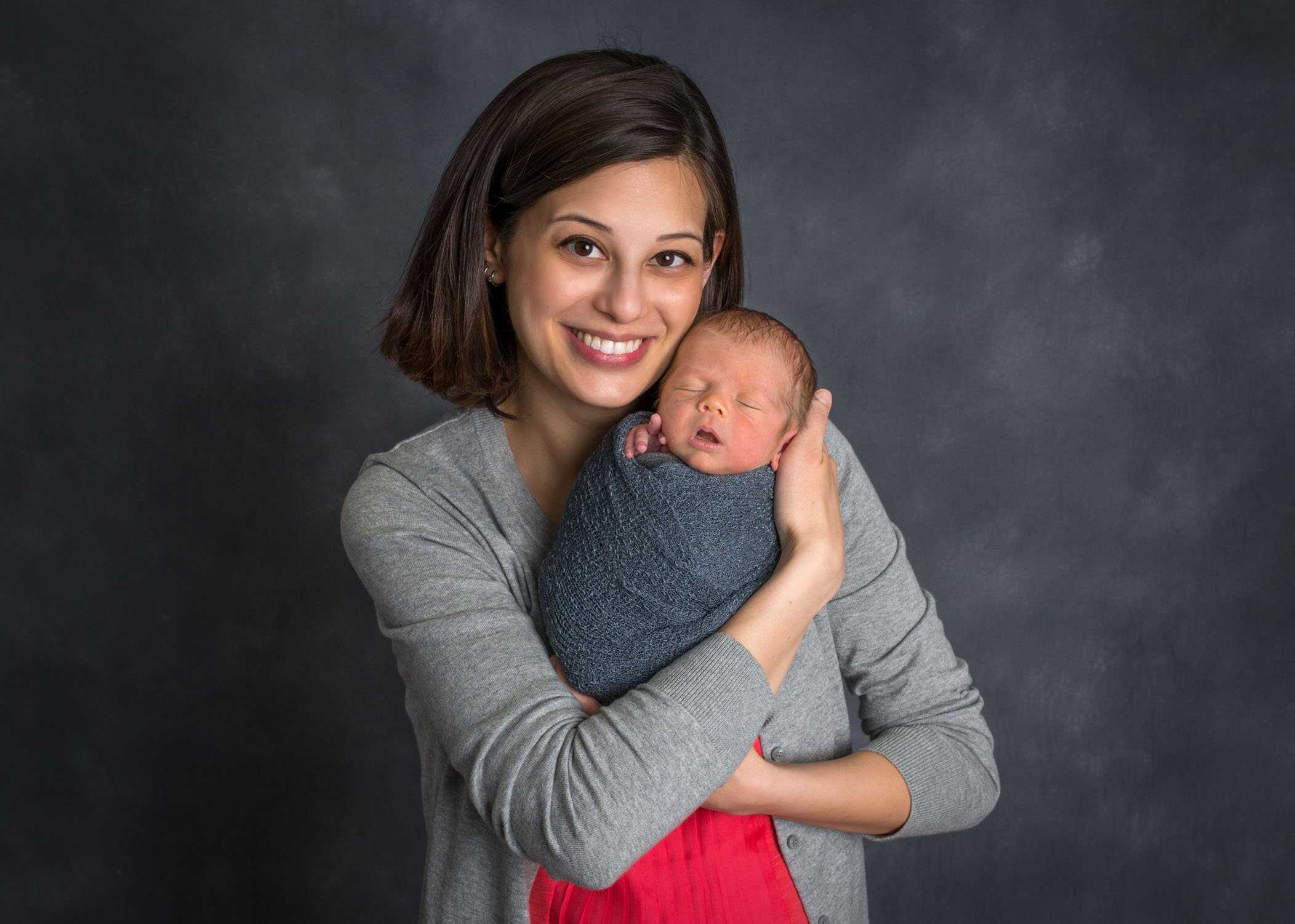 Mom holds newborn son cheek to cheek and smiles