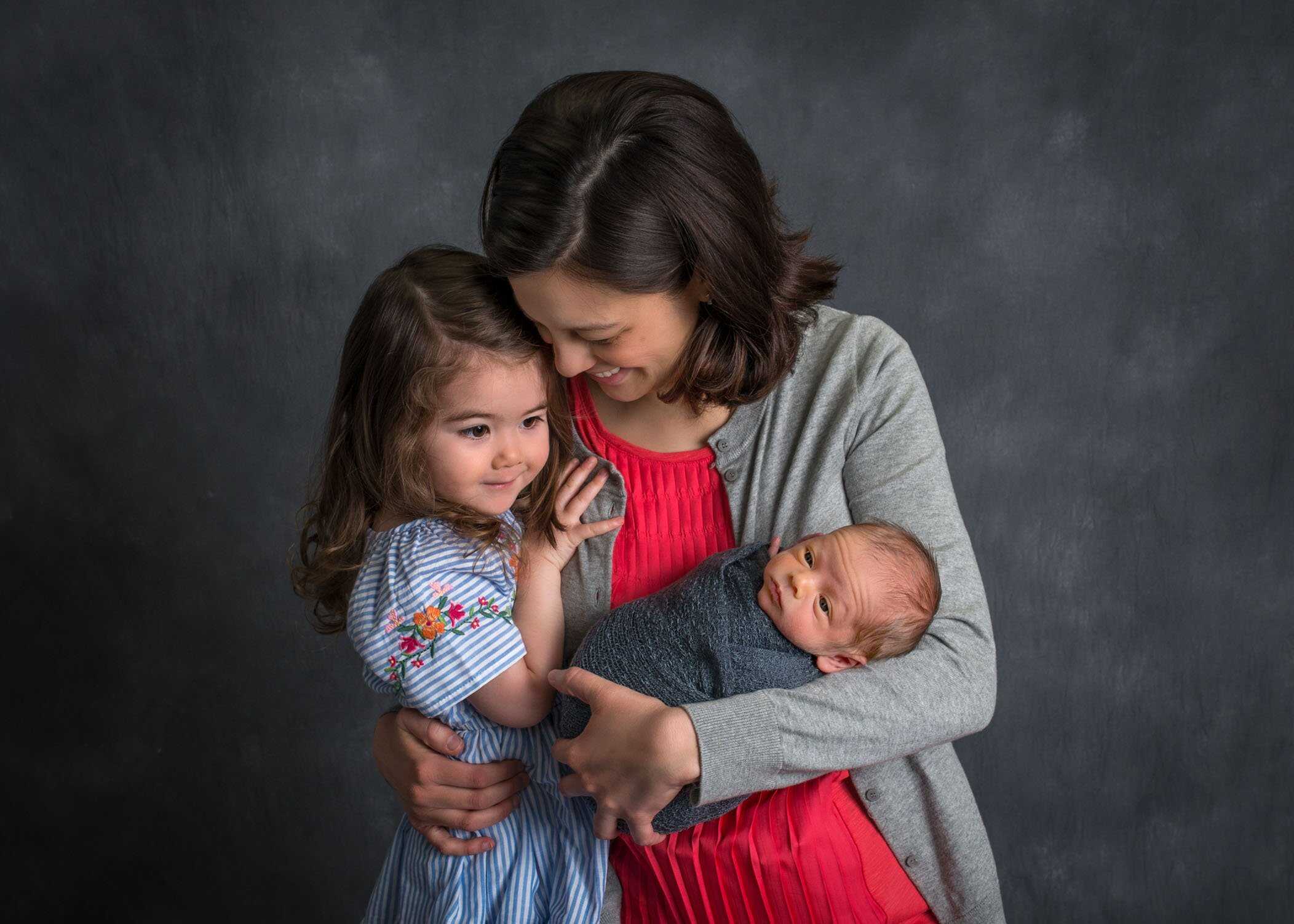 Mom hugs both her toddler daughter and newborn son