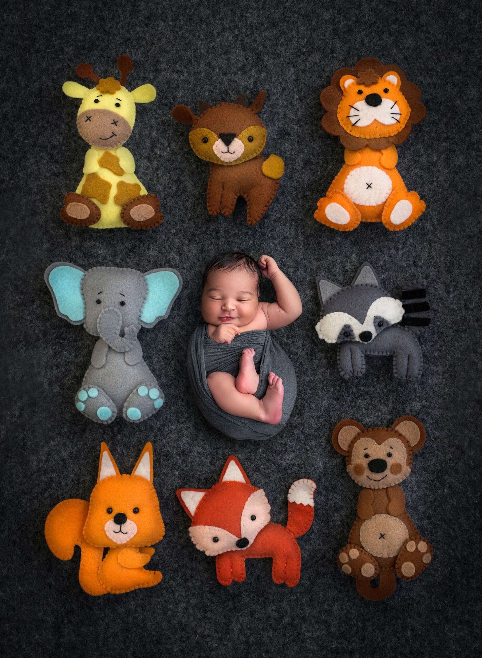 newborn baby boy swaddled in grey in the middle of stuffed animals