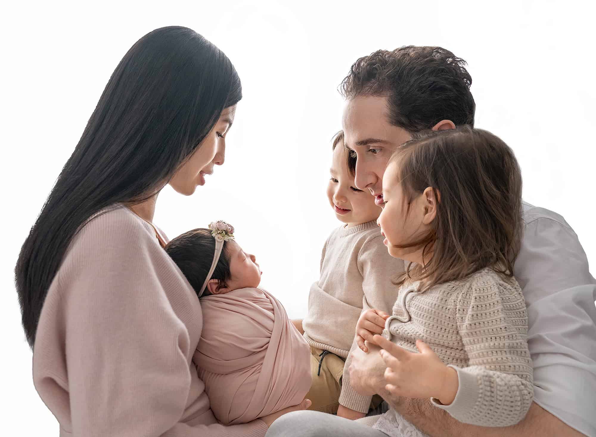 Family facing inward, parents and two children admiring the sleeping newborn.