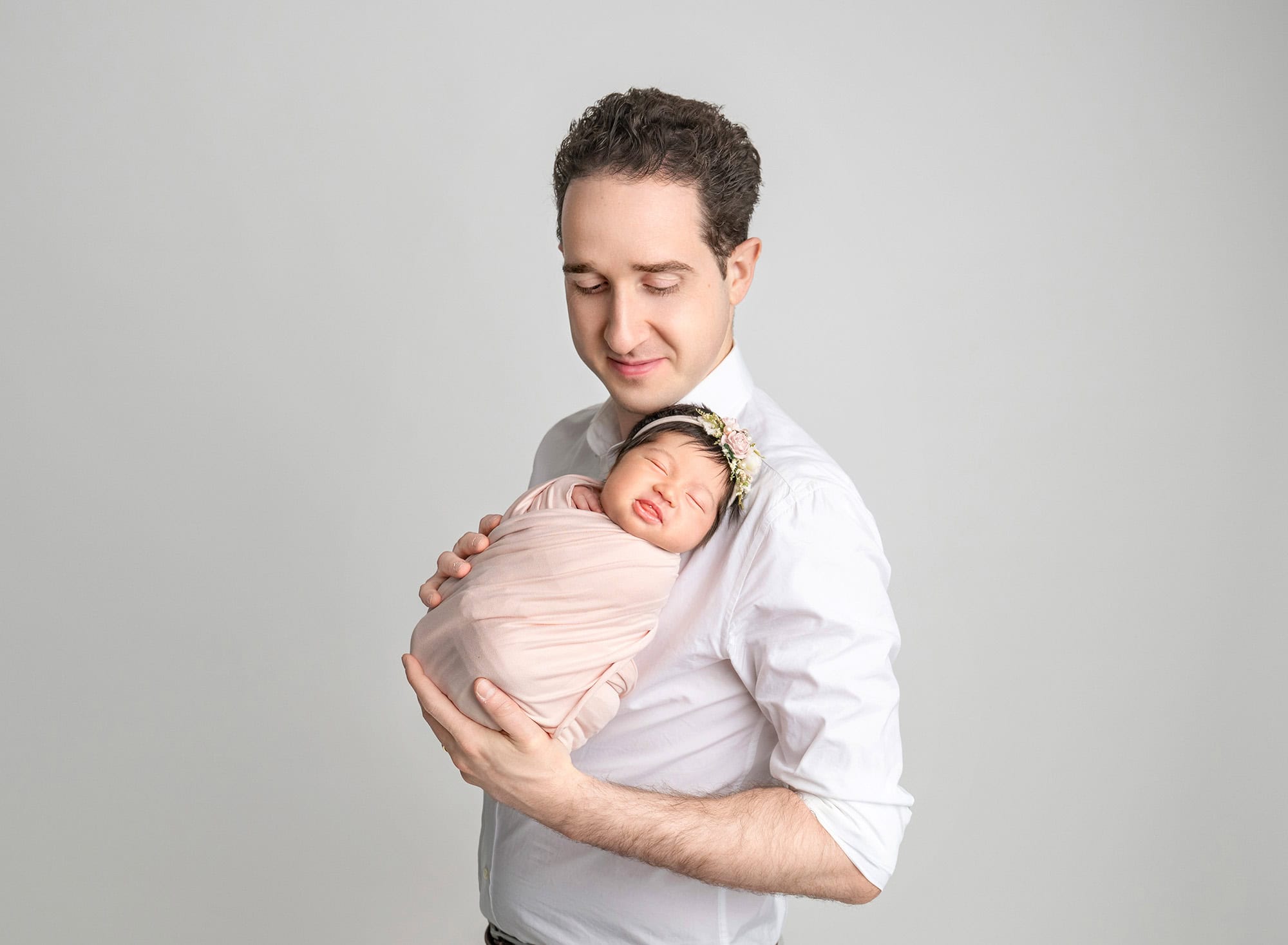 father cradling peacefully sleeping newborn in blush wrap, bright studio light.
