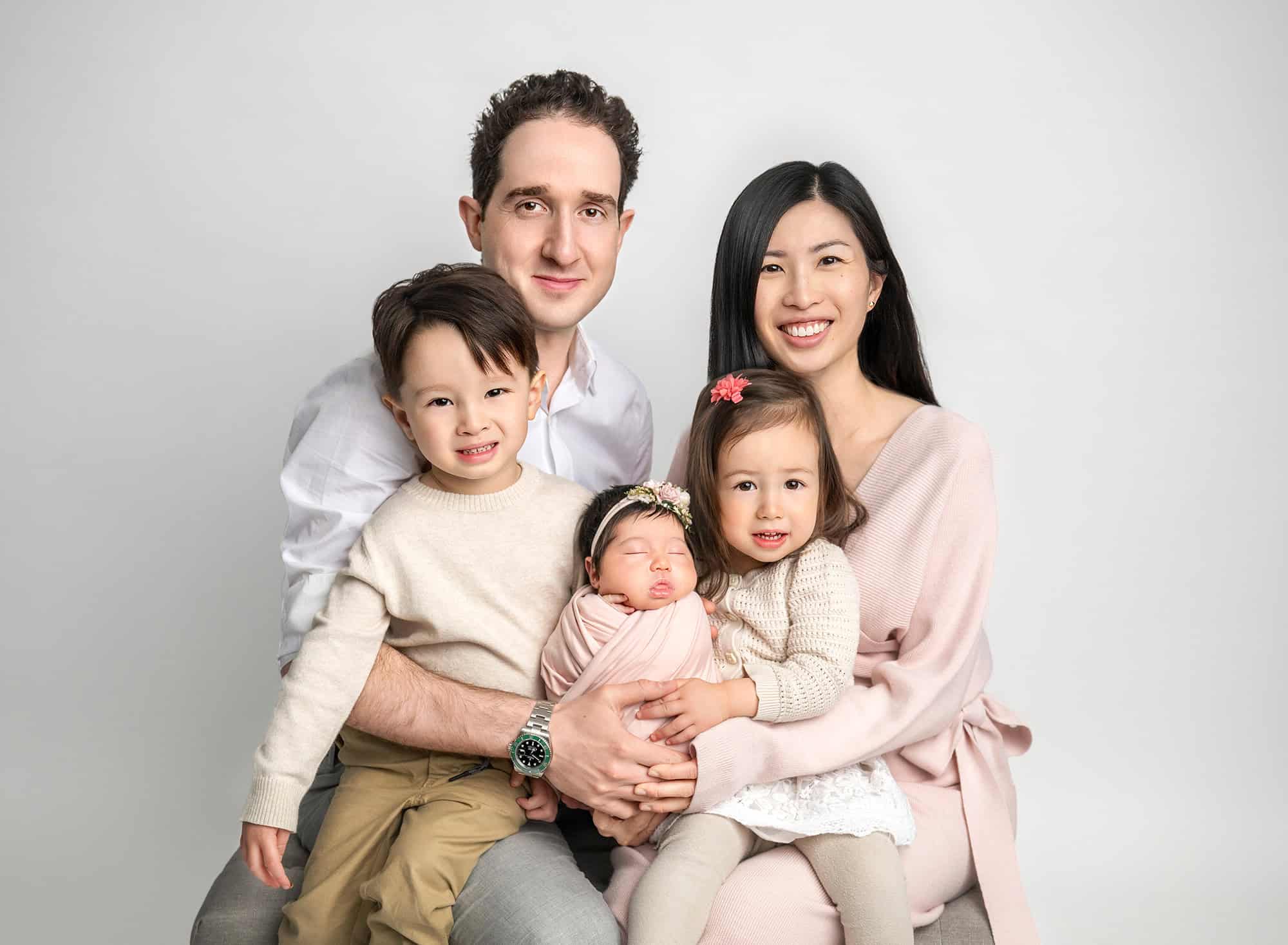 Studio family portrait with parents and three children seated, neutral outfits.