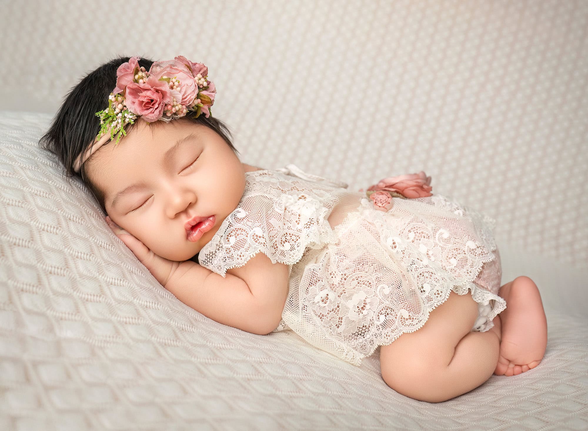 Sleeping newborn in lace outfit on neutral backdrop, gentle side light.