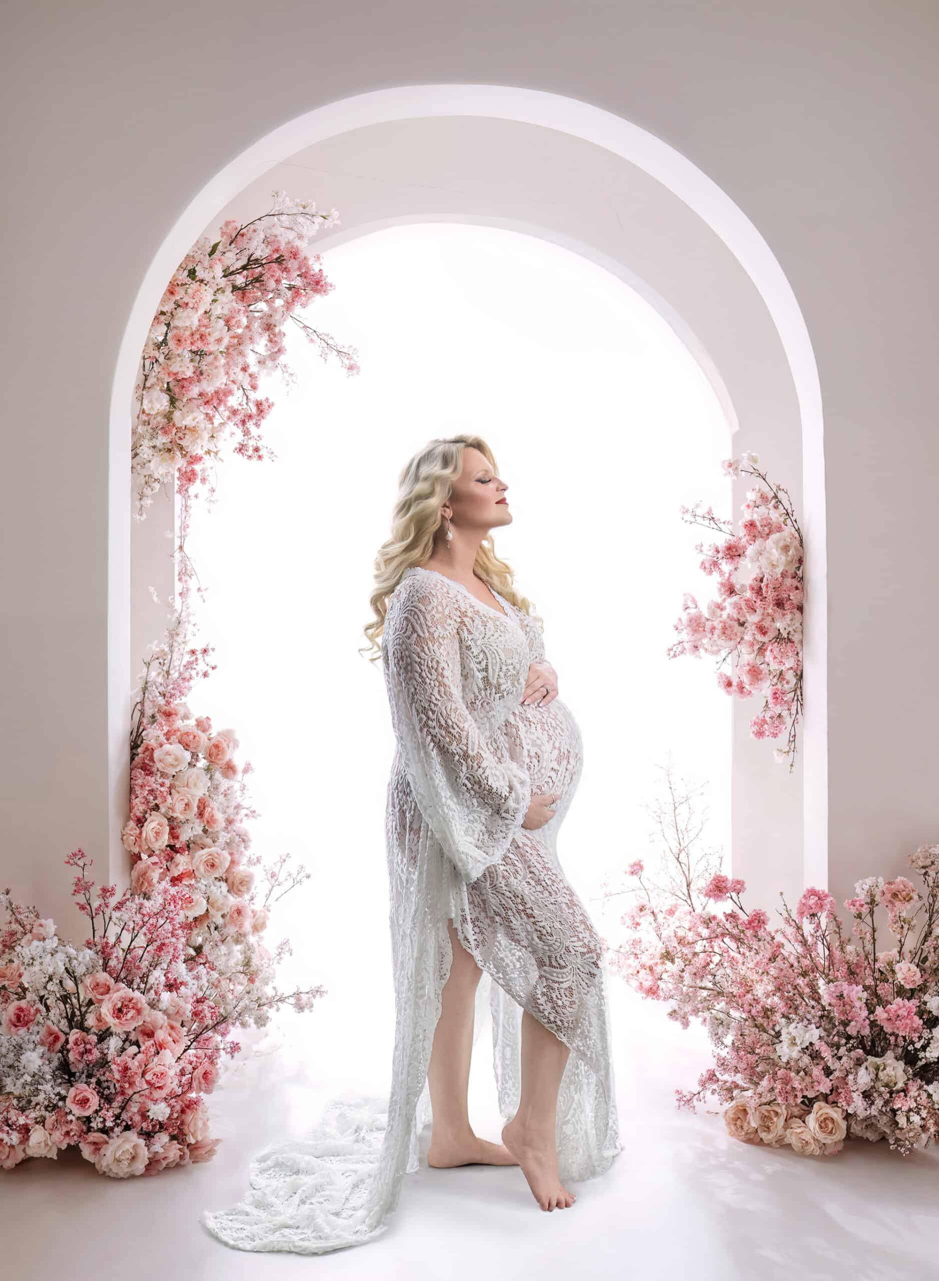 pregnant mom backlit in front of white archway covered in pink roses