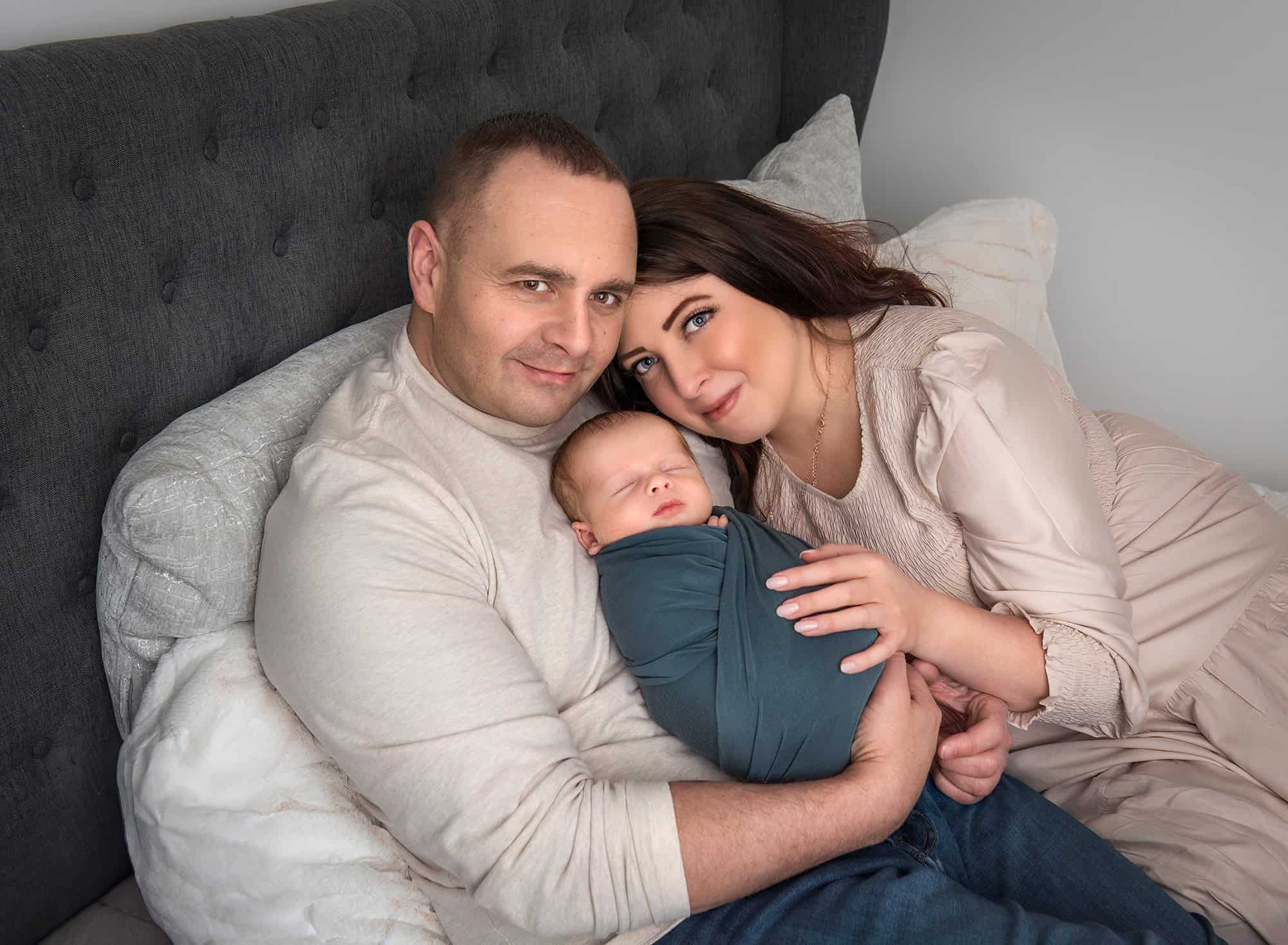 Unique Newborn Photography with Parents Parents snuggling their newborn baby boy on a bed