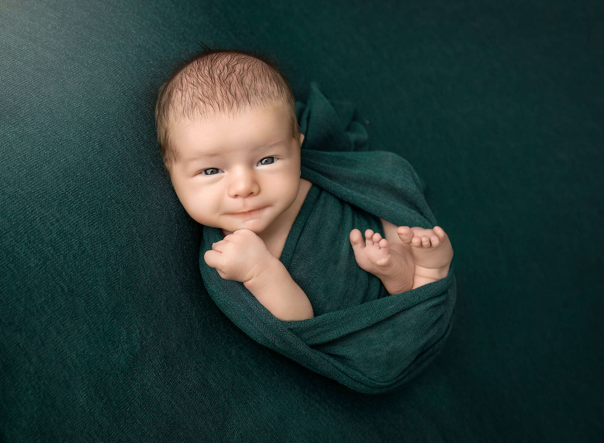 Leif in deep-green wrap with tiny toes peeking on matching backdrop