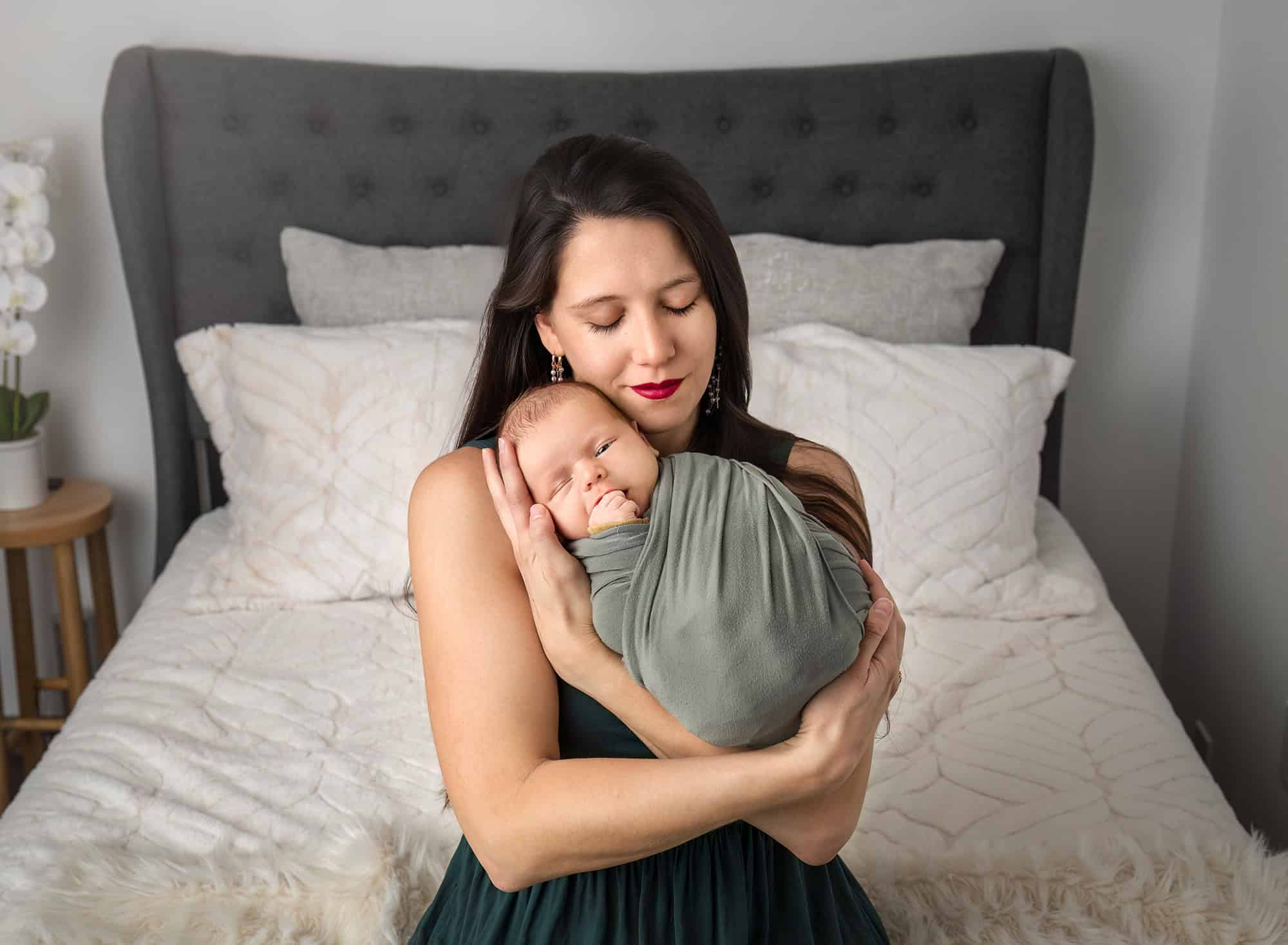 newborn photos with dogs—mother cuddling swaddled Leif on the bed, peaceful portrait