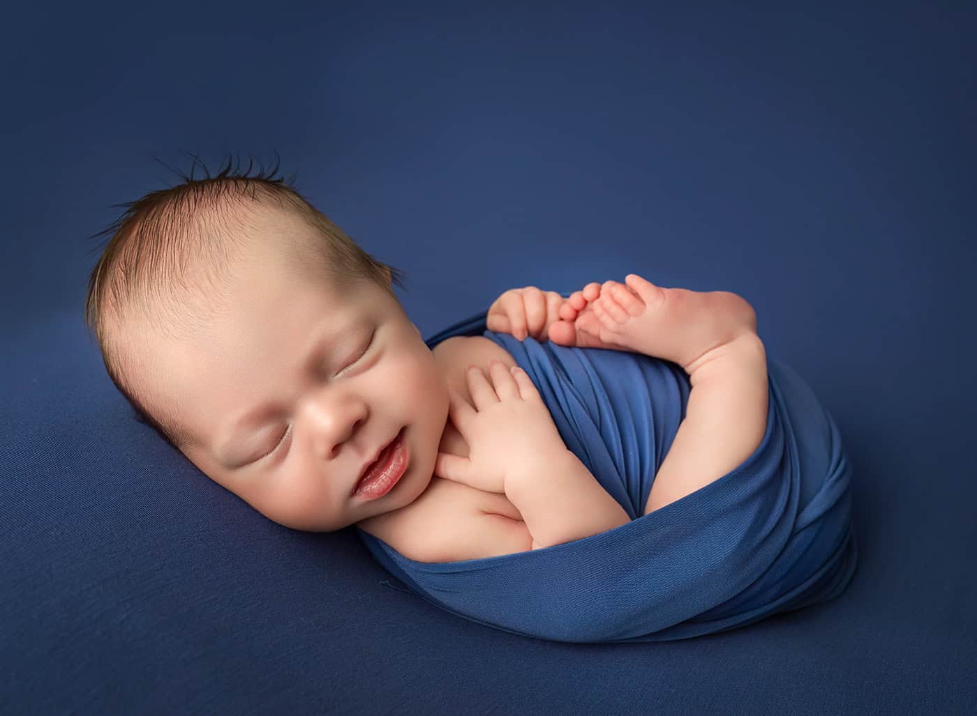 newborn boy photos sleeping wrapped up with a grin on his face