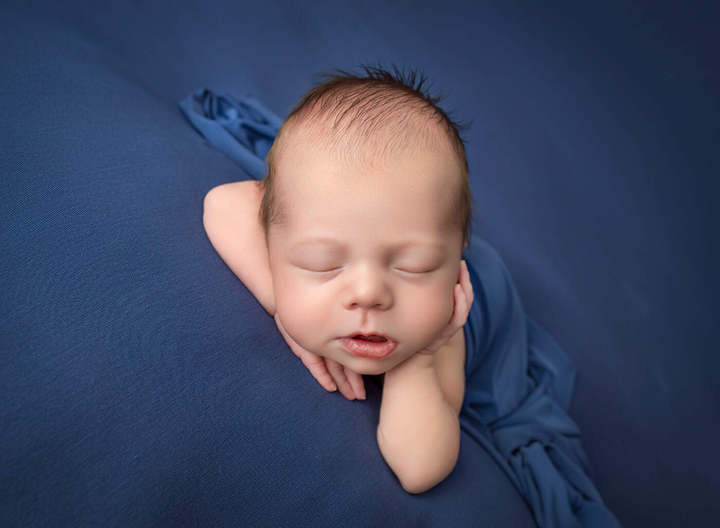 newborn boy photos baby boy sleeping with his hand cupping his cheek on a blue blanket