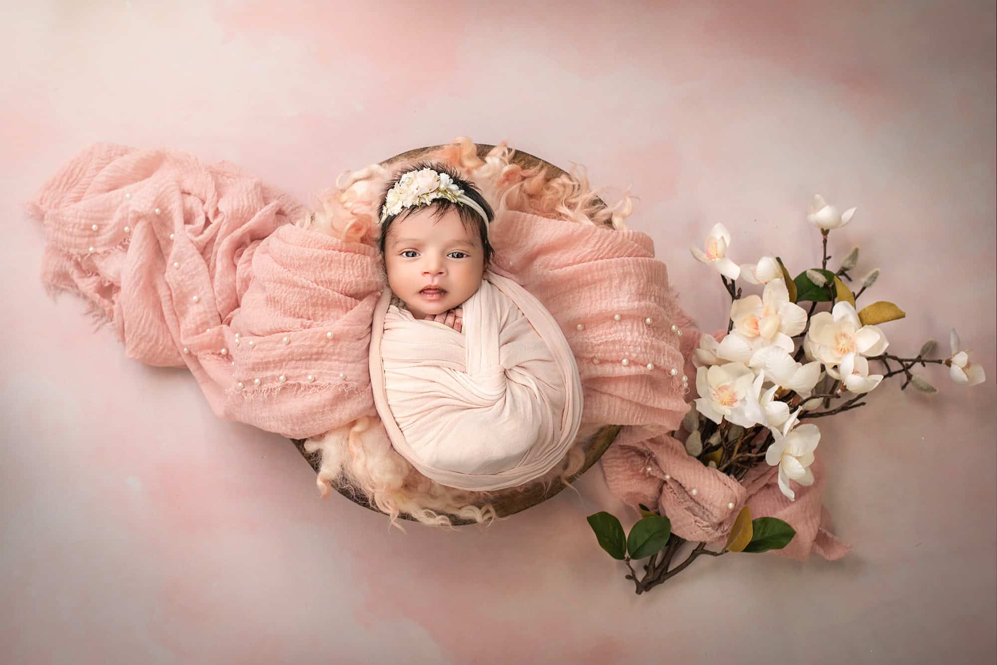 Luxury Newborn Photographer Glastonbury CT Wide-eyed baby in a rustic bowl with pink tones and white florals