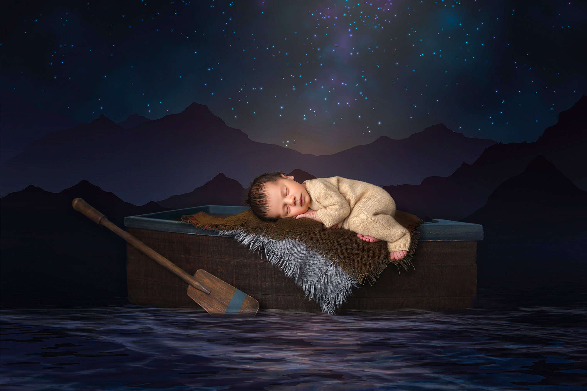 High-End Newborn Photography Connecticut tiny newborn boy sleeping on a rowboat on a lake in the mountains with starlight behind him