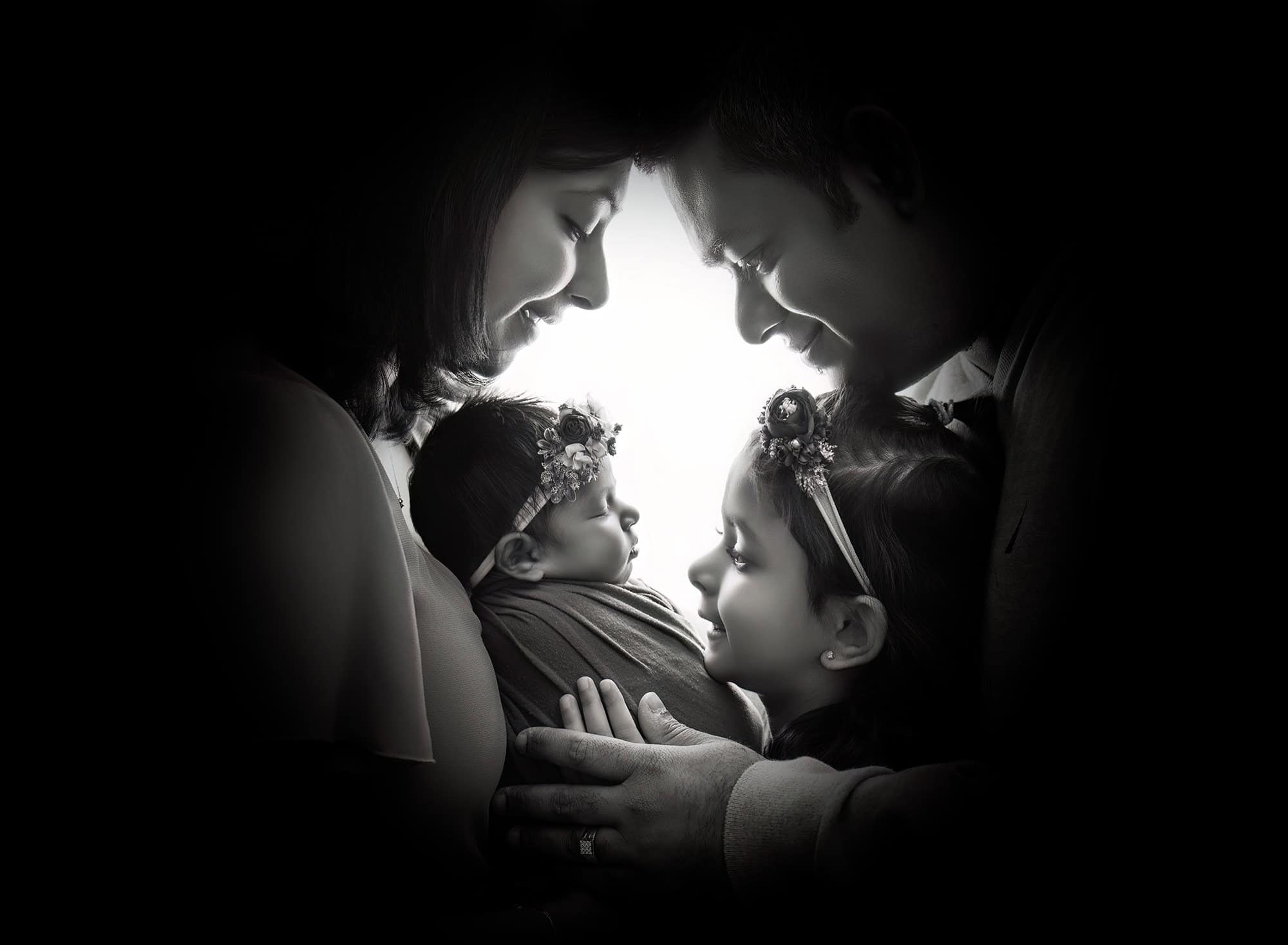 Family of four looking down at baby in black and white