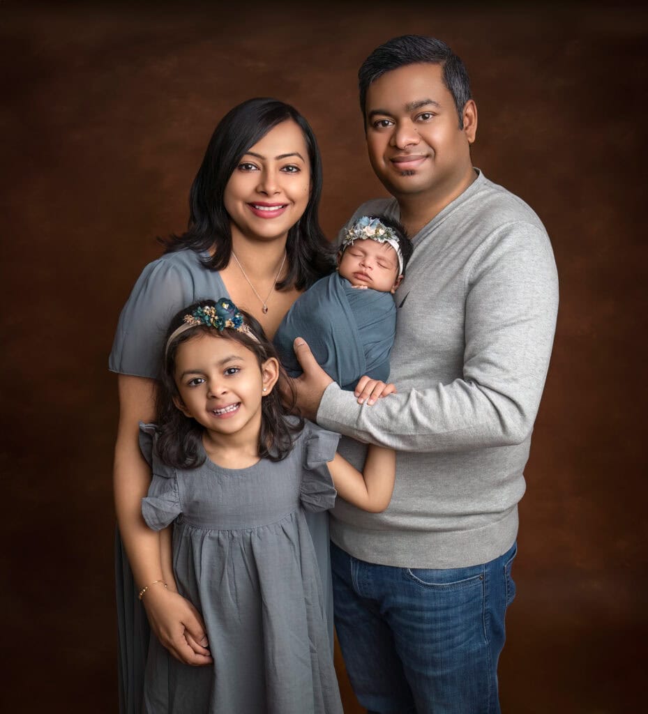 newborn photos what to wear Traditional studio portrait of family of four on a brown background