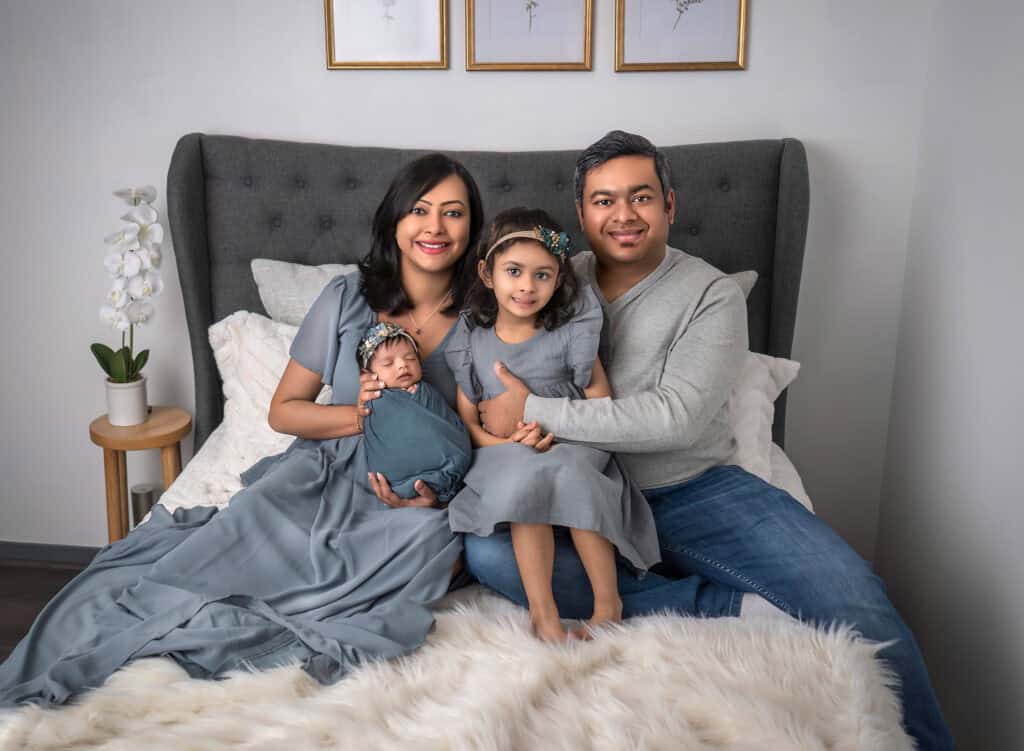 Family dressed in blue, sitting on a bed together with newborn