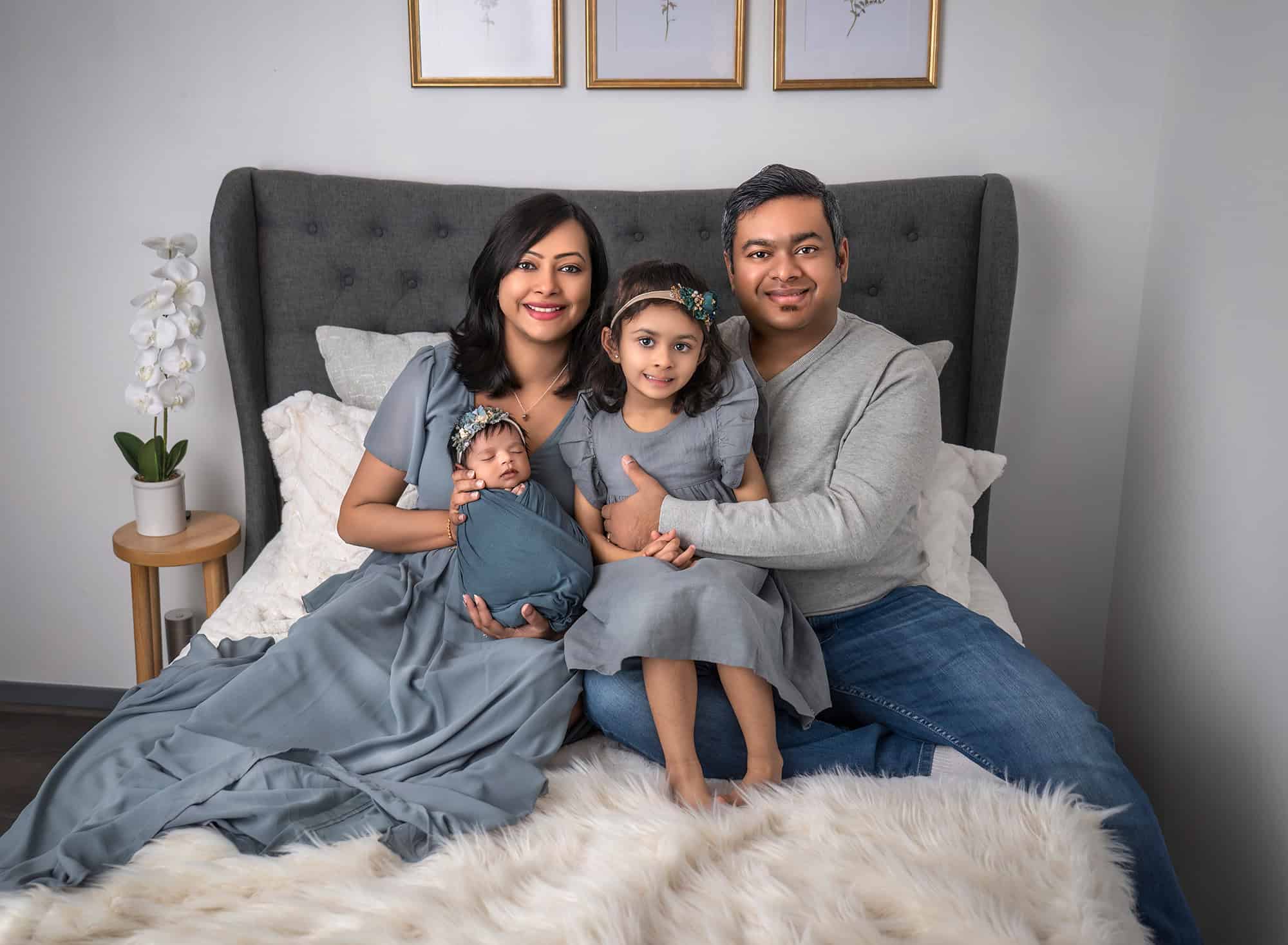 Family dressed in blue, sitting on a bed together with newborn