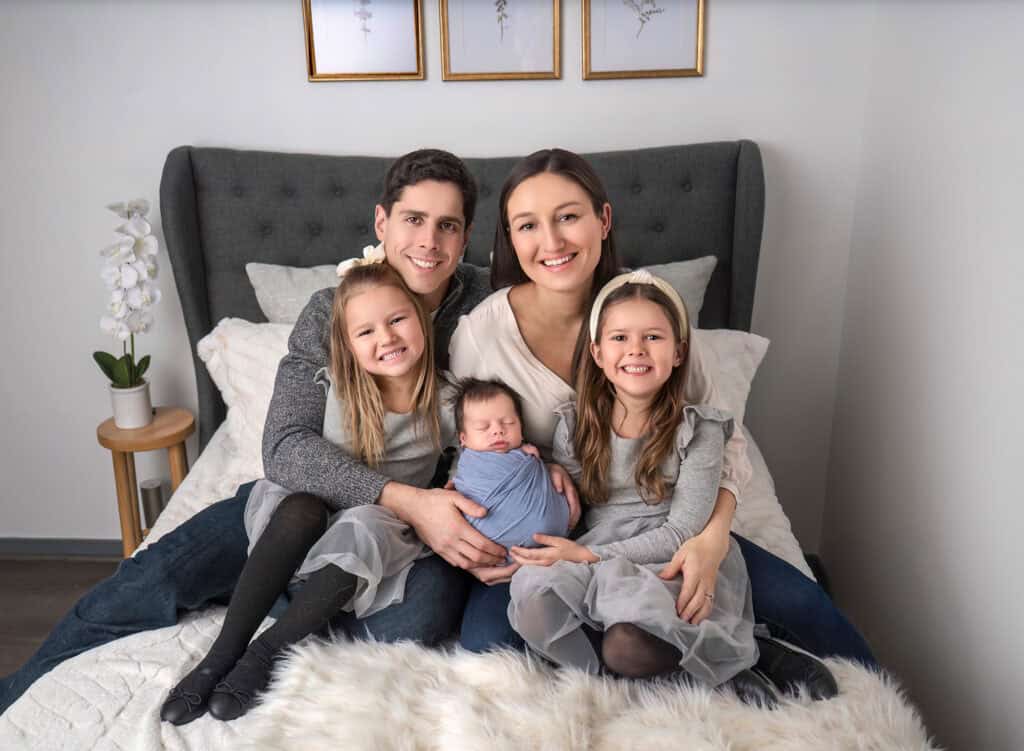 newborn photos what to wear Family portrait of 5, consisting of 2 daughters and newborn baby boy sitting on a bed