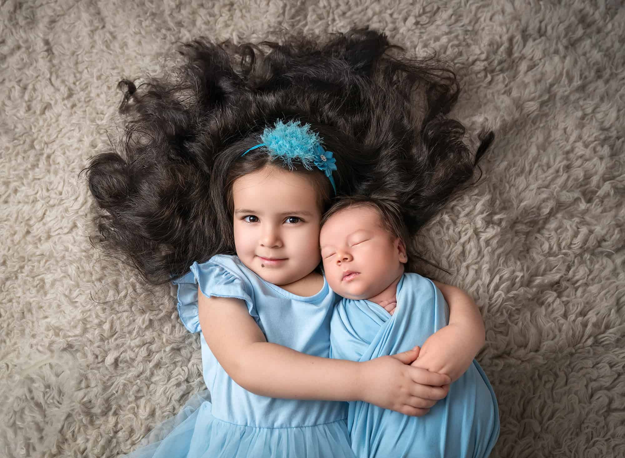 Kalina cuddling newborn Roman while lying on a cozy rug.