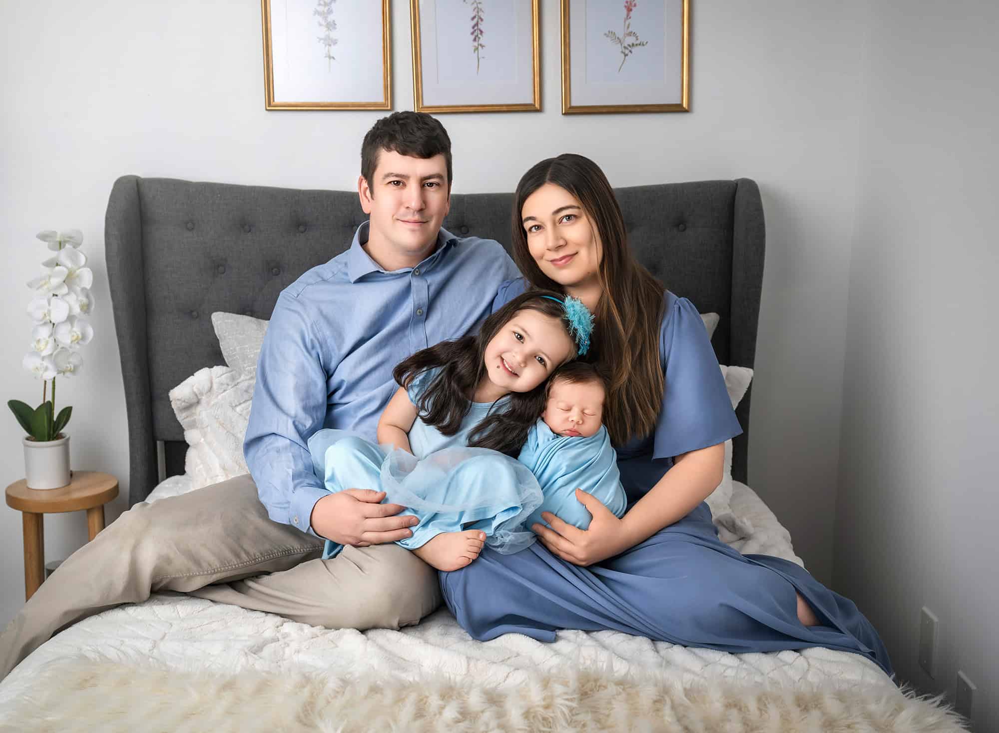 Parents on bed holding daughter and sleeping baby for newborn pictures.