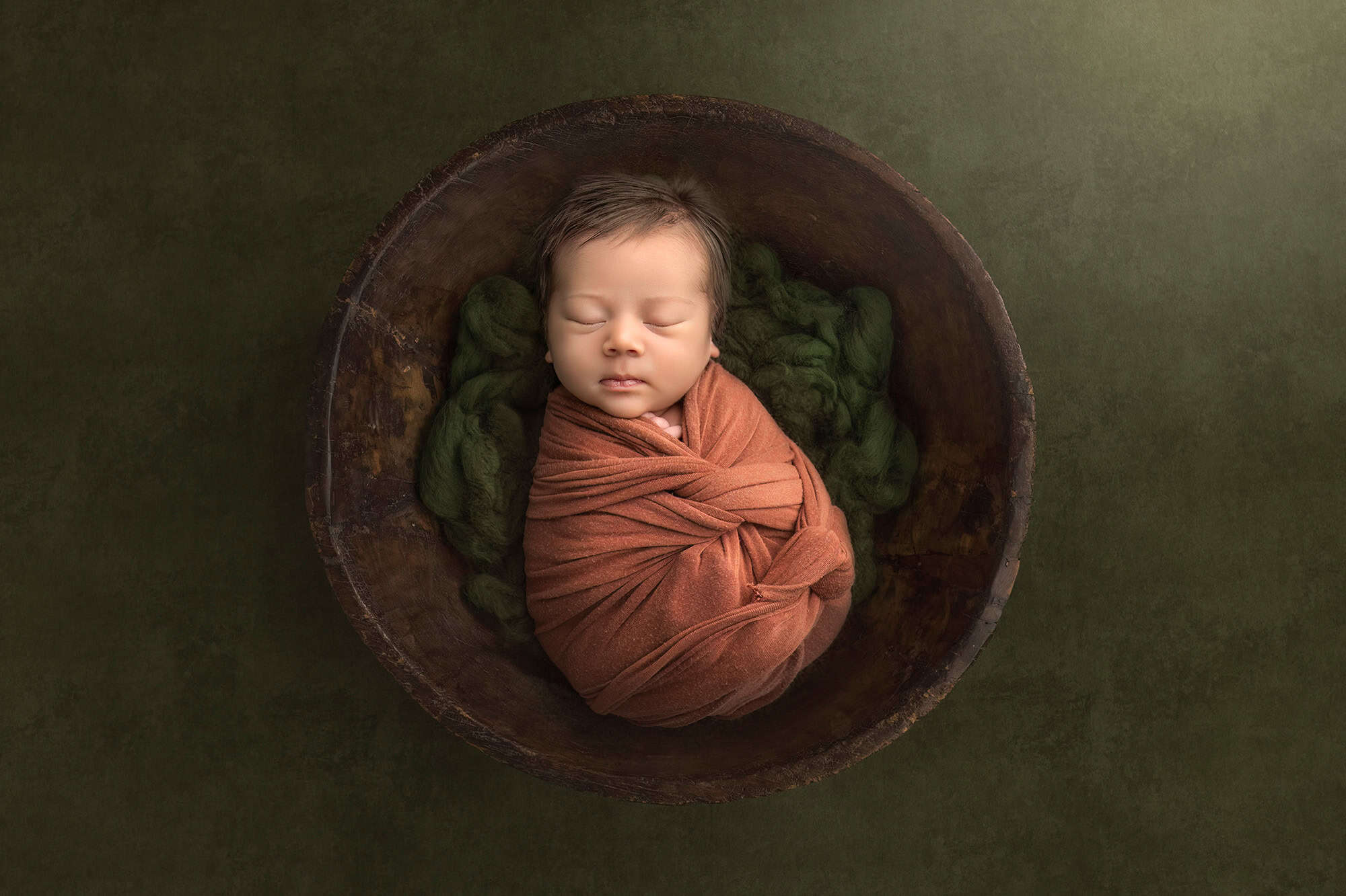 Newborn Roman swaddled in rust wrap inside wooden bowl.
