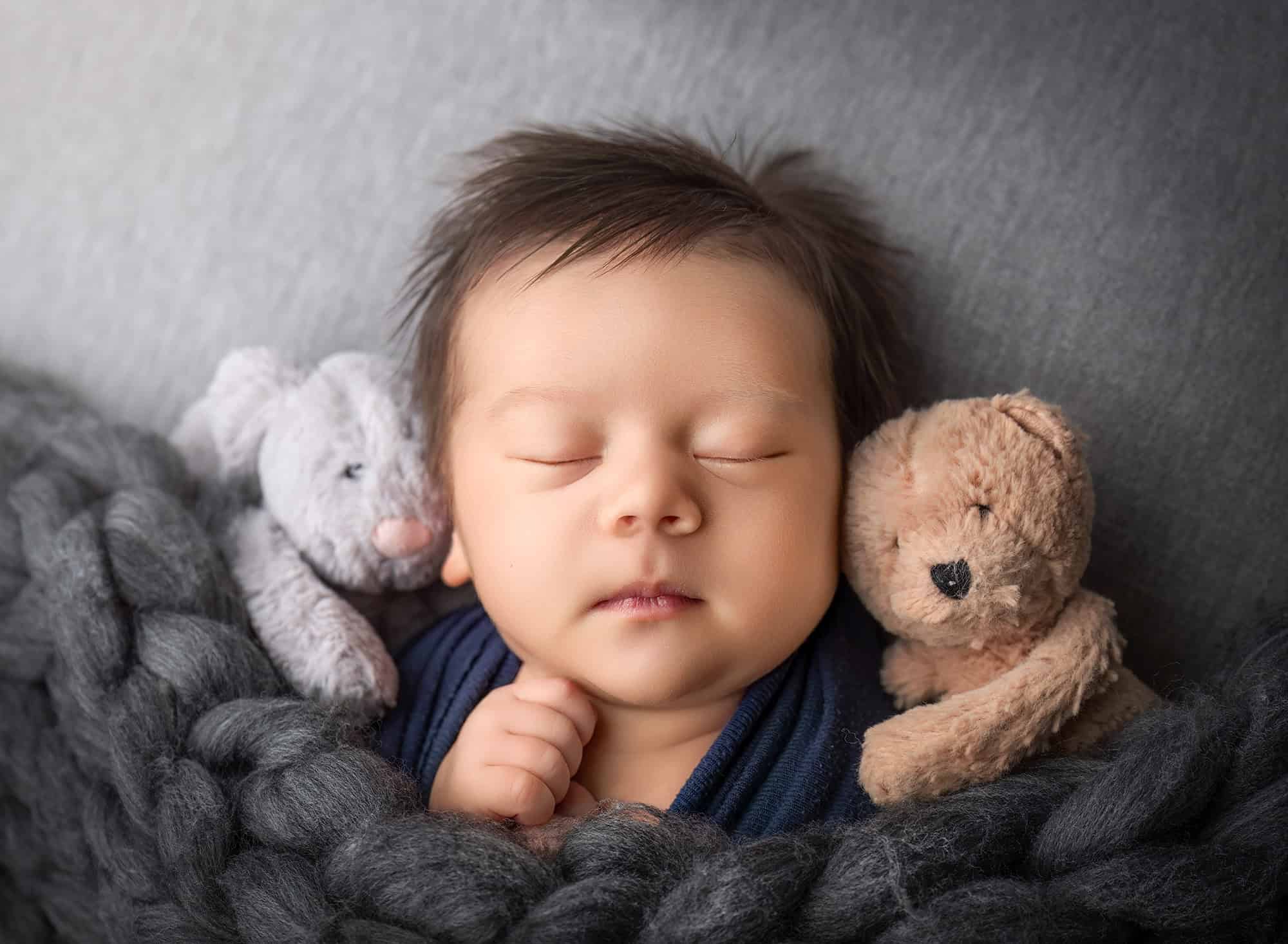 Close-up of sleeping baby with two small teddy friends.