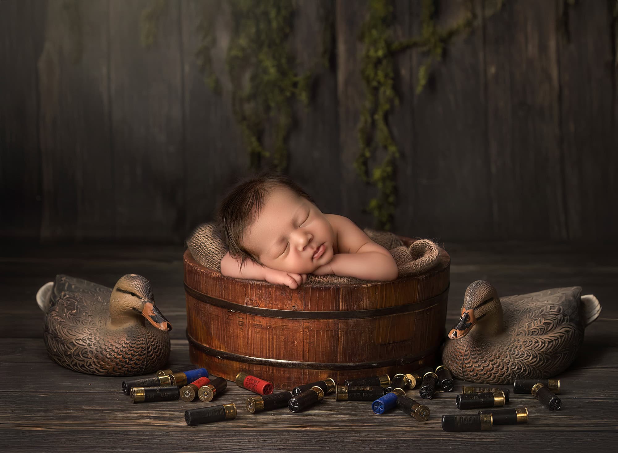 Duck-hunting themed newborn photograph with decoys and wooden tub.