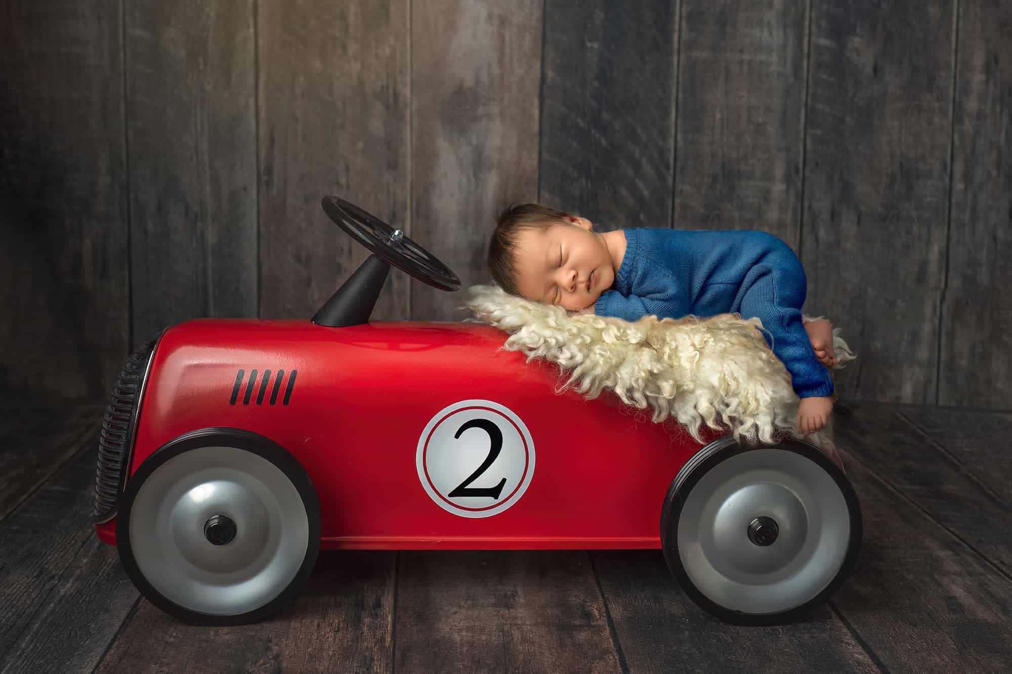 Newborn napping on red vintage toy car.